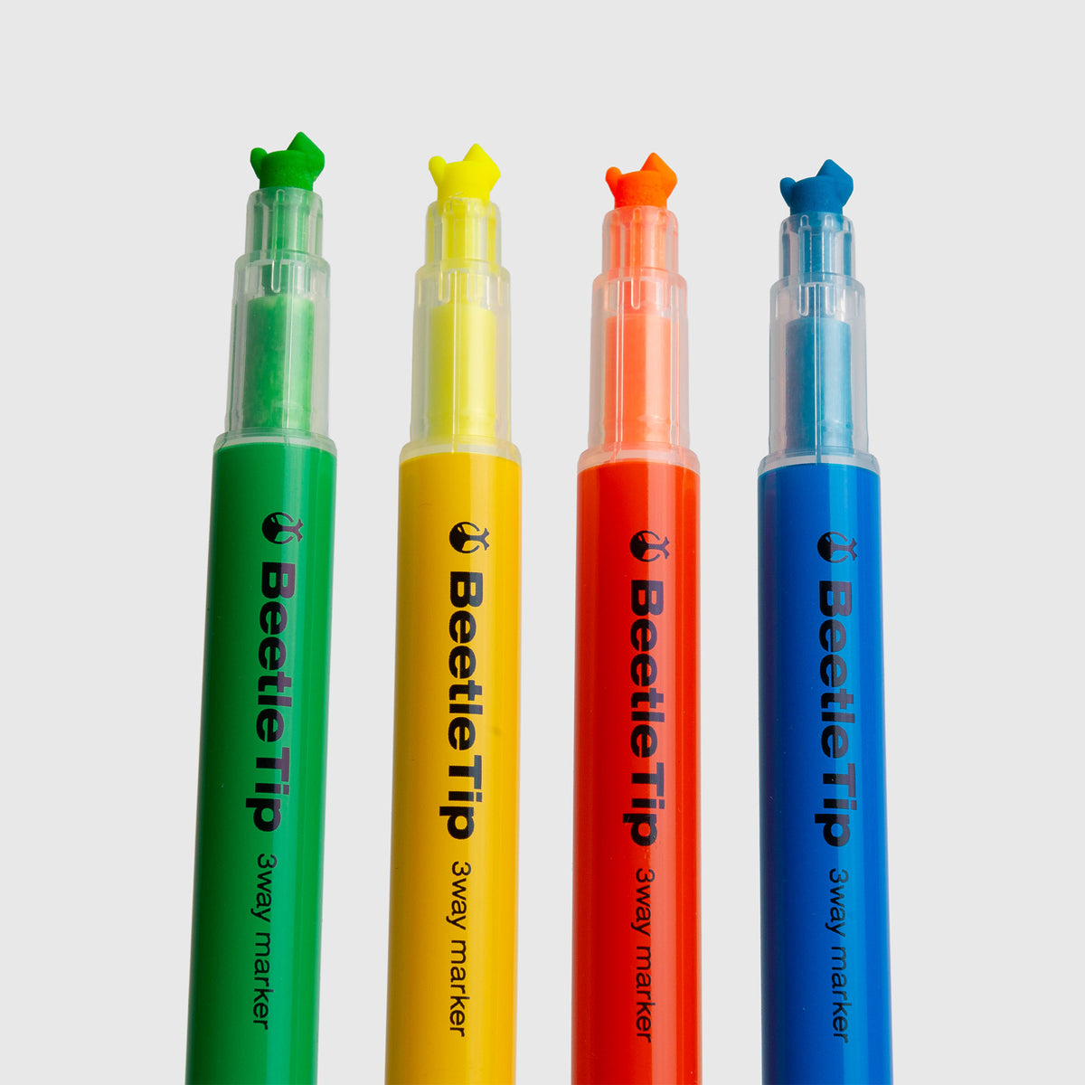 Vier Kokuyo Beetletip 3-Way-Textmarker – Textmarker mit drei Spitzen in Grün, Gelb, Orange und Blau stehen mit ihren farbigen Spitzen und transparenten Kappen in einer Reihe auf einem hellen Hintergrund – ideal für Fans der Beetletip-Serie der Marke Kokuyo.