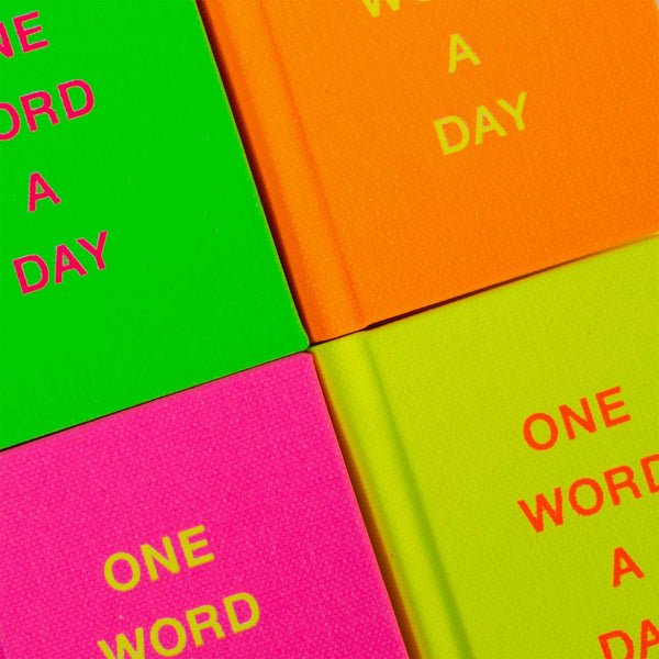 Vier farbenfrohe OWAD Neon-Notizbücher von paperlux.store bilden ein Quadrat. Oben links ist grün, oben rechts ist orange, unten links ist rosa und unten rechts ist gelb – jedes trägt in leuchtendem Text die Aufschrift „ONE WORD A DAY“. Ein echtes Bestseller-Geschenk-Feeling!.