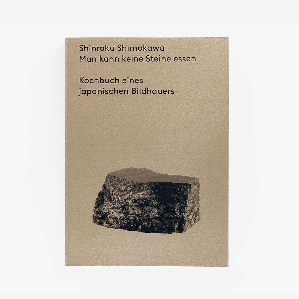 Der Buchumschlag zeigt einen beigen Hintergrund und ein schwarz-weißes Steinbild. Der Text enthält den Namen des Autors „Shinroku Shimokawa“ und den Titel „Man kann keine Steine essen“ mit dem Untertitel „Kochbuch eines japanischen Bildhauers“, wobei der Schwerpunkt auf regionalen Zutaten für ein authentisches japanisches Kocherlebnis liegt. Veröffentlicht von Prima Publikationen.