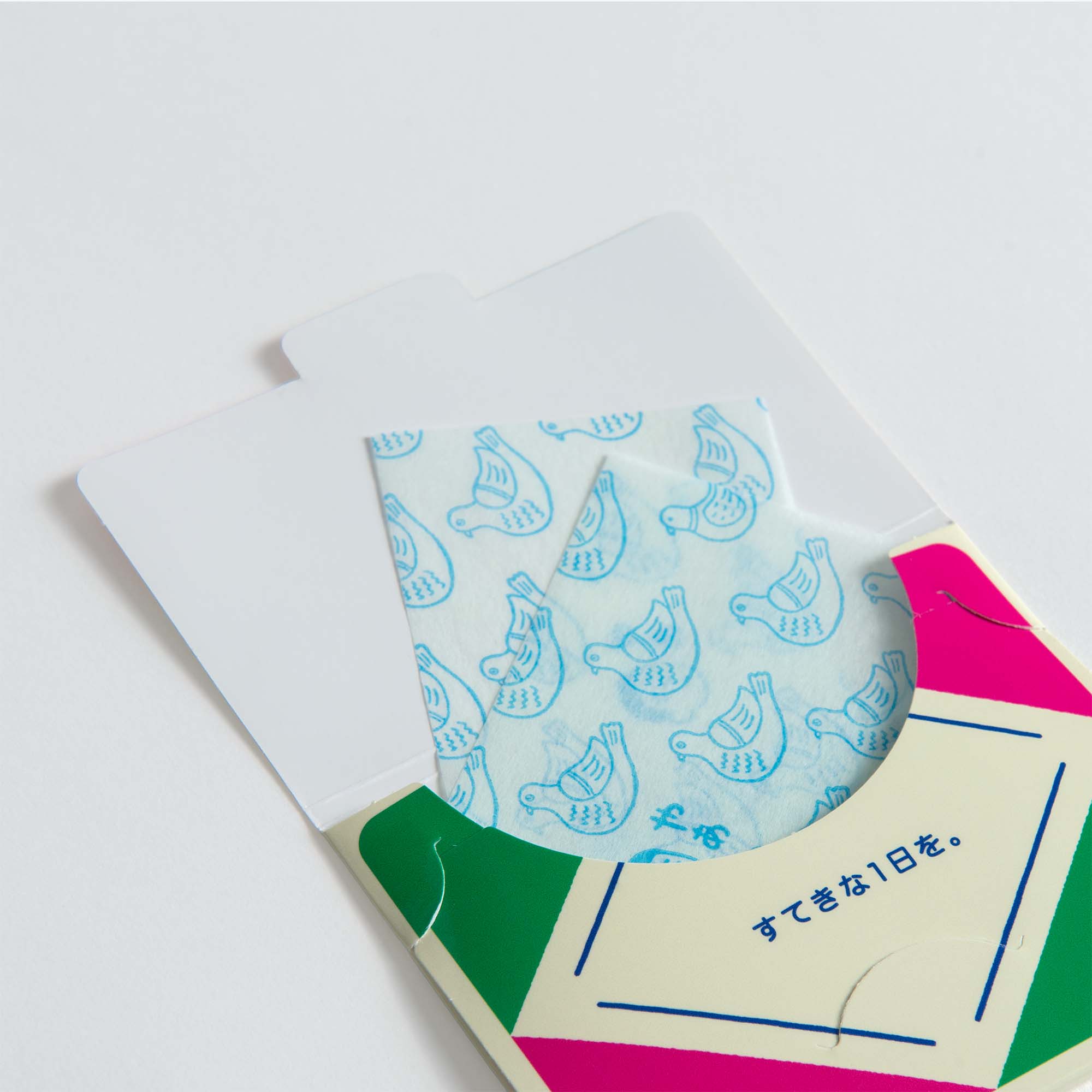 Eine farbenfrohe Hightide-Papierseifen-Verpackung mit geometrischen Mustern enthüllt ein dünnes Blatt, das mit blauer Vogelkunst und japanischem Text verziert ist - ein Retro-Design-Touch, perfekt für Reisen.