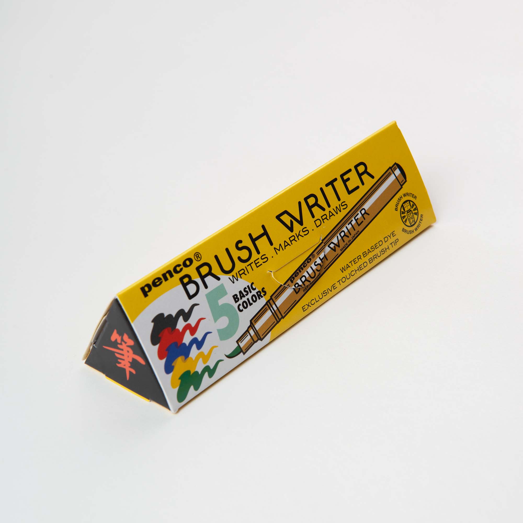 Eine gelbe dreieckige Schachtel mit der Aufschrift "Penco Brushwriter-Set aus 5 Farben" zeigt bunte Pinselstriche und eine Stiftabbildung. Das in Japan hergestellte Set ist ideal für Kalligrafie-Pinsel oder Aquarell-Effekte - schreibt, markiert und zeichnet in 5 Grundfarben.