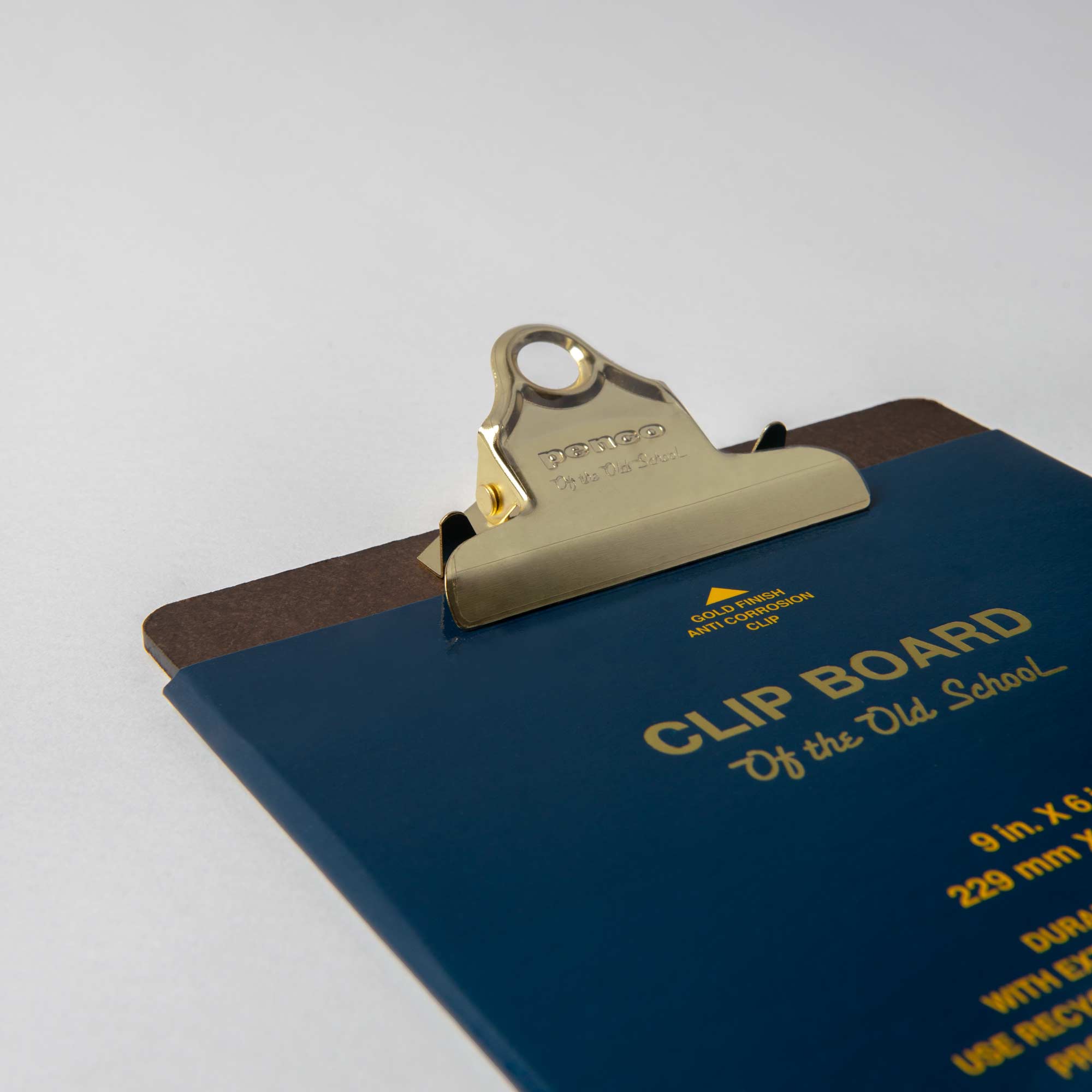 Ein teilweise abgebildetes Penco A5-Klemmbrett weist ein blau-braunes Design mit einem goldenen Metallclip auf. Der Text „CLIP BOARD Of the Old School“ erscheint in Gelb neben Maß- und Materialangaben. Perfekt für Organizer, bietet es Vintage-Charme vor einem neutralen Hintergrund.