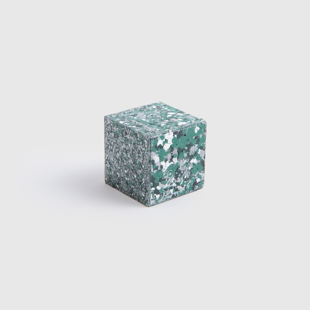 Ein kleines, grün-weiß gesprenkeltes „Color Gem“ – das Wachsmalquadrat – Einzelpackung von Studio Unto, inspiriert von „Zeichnen aus der Natur“, liegt auf einem schlichten weißen Hintergrund.