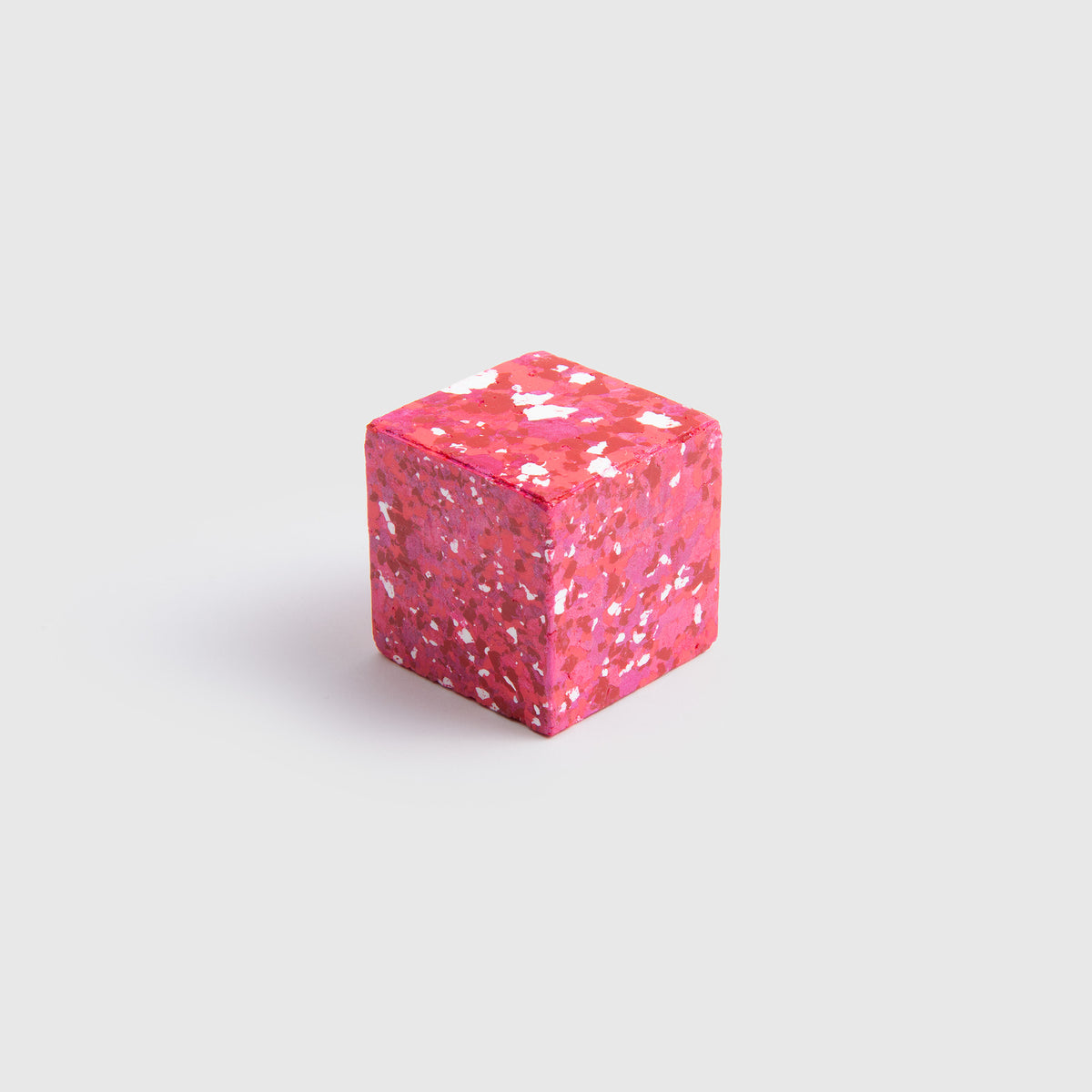 Ein kleiner rosa Würfel – Color Gem – das Wachsmalquadrat – Einzelpackung von Studio Unto – mit einem weiß und dunkelrosa gesprenkelten Muster liegt auf einem hellgrauen Hintergrund und eignet sich ideal als Inspiration für das Zeichnen nach der Natur oder zum Gestalten eigener Kunstwerke.