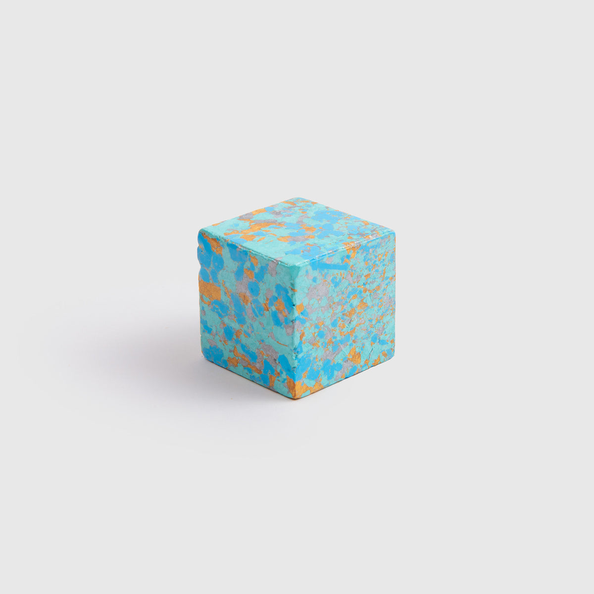 Ein kleiner Würfel von Studio Unto namens „Color Gem – das Wachsmalquadrat – Einzelpackung“ mit einem türkis-orange gesprenkelten Muster, das von „Zeichnen aus der Natur“ inspiriert ist, liegt auf einem schlichten weißen Hintergrund und wartet darauf, zur Gestaltung neuer Kunstwerke anzuregen.