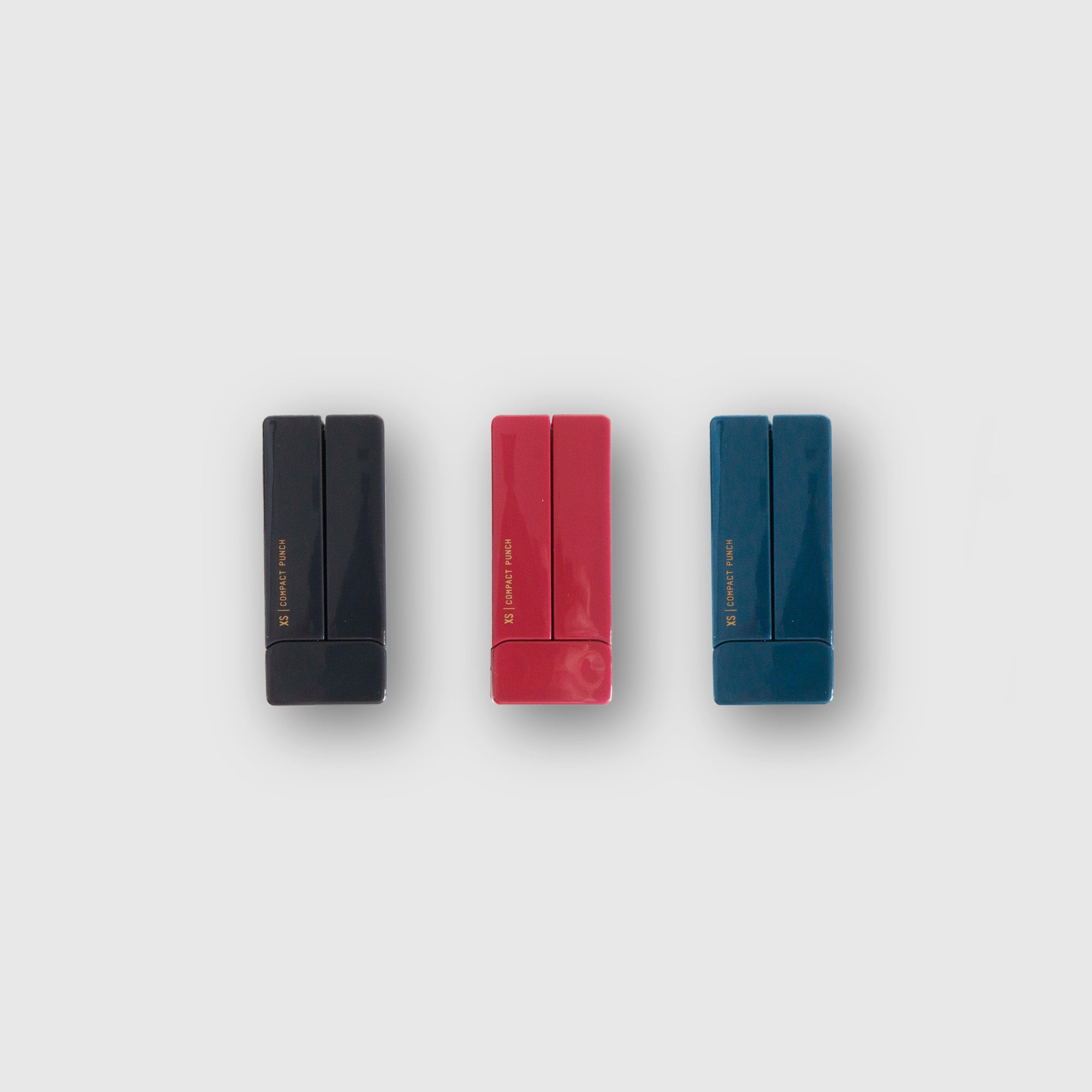 Drei rechteckige Textmarker in Schwarz, Rot und Blau stehen nebeneinander aufrecht auf einem schlichten hellgrauen Hintergrund – ideale Begleiter für Ihren Schreibtisch zusammen mit dem Midori XS Compact Punch von Midori.