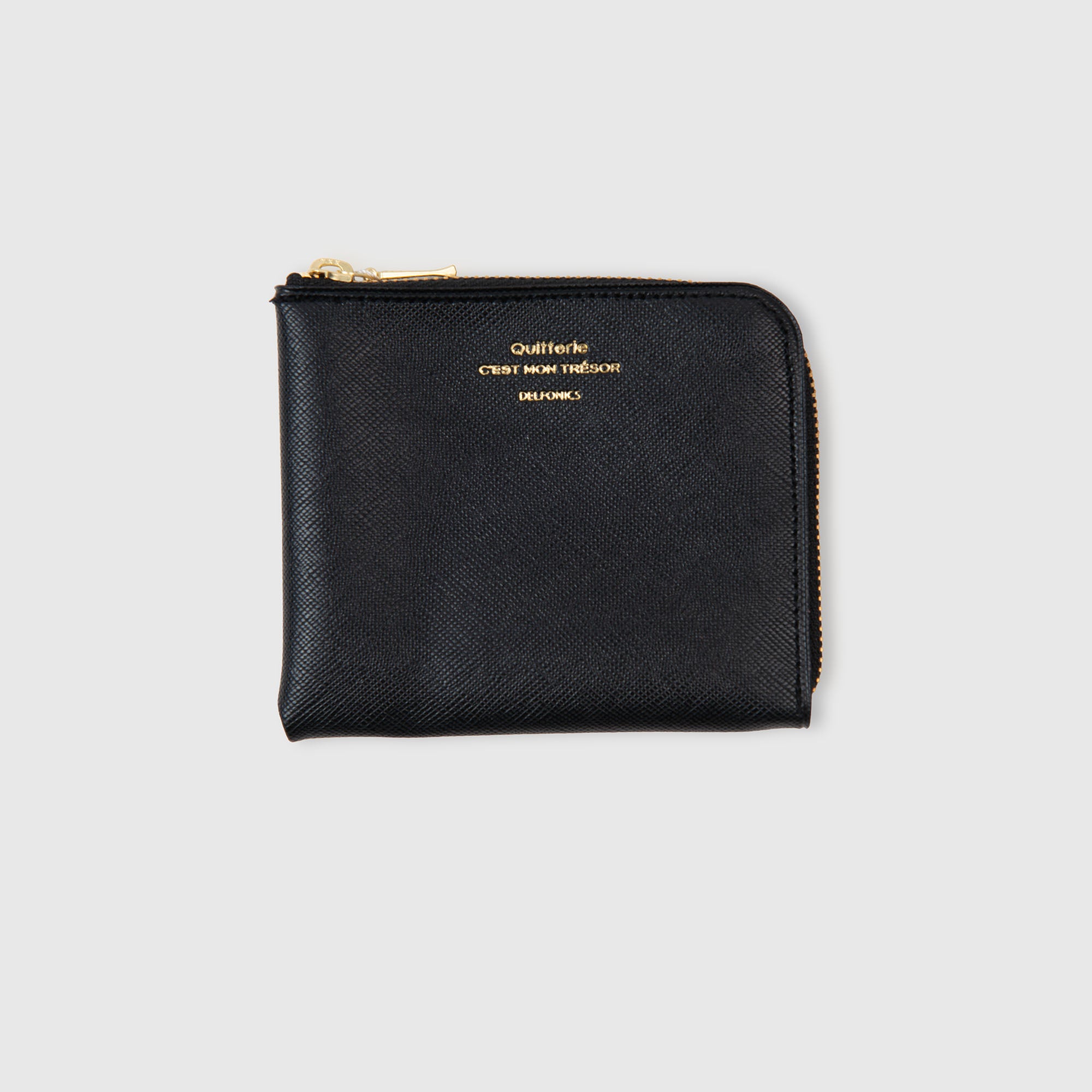 Ein schwarzes Kartenetui aus Leder mit Reißverschluss und goldenen Akzenten, gefertigt in Scotch-Grain-Optik und vor einem schlichten hellgrauen Hintergrund präsentiert. Das Delfonics Quitterie Half Zip Card Case | Kartenetui ist zudem wasserabweisend und vereint Stil und Funktionalität der renommierten Marke Delfonics.