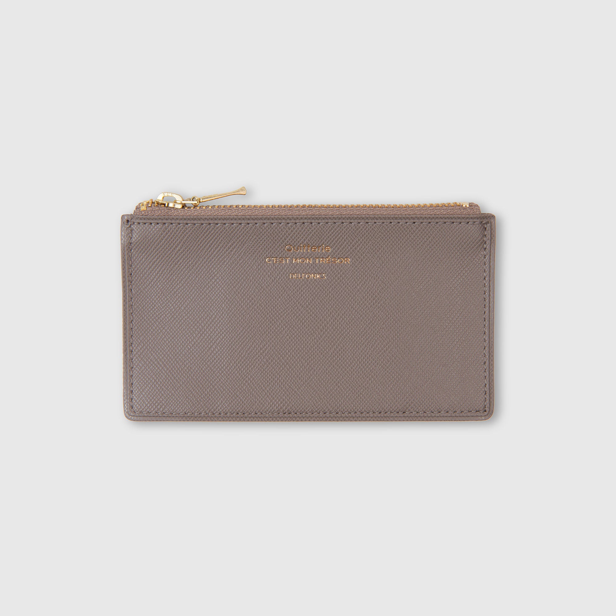 Ein taupefarbenes Leder-Kartenetui „Quitterie Card Zip Case“ von Delfonics | Kartenetui von Delfonics mit goldenem Reißverschluss und geprägtem goldenem Schriftzug auf der Vorderseite, dargestellt vor einem schlichten hellgrauen Hintergrund.