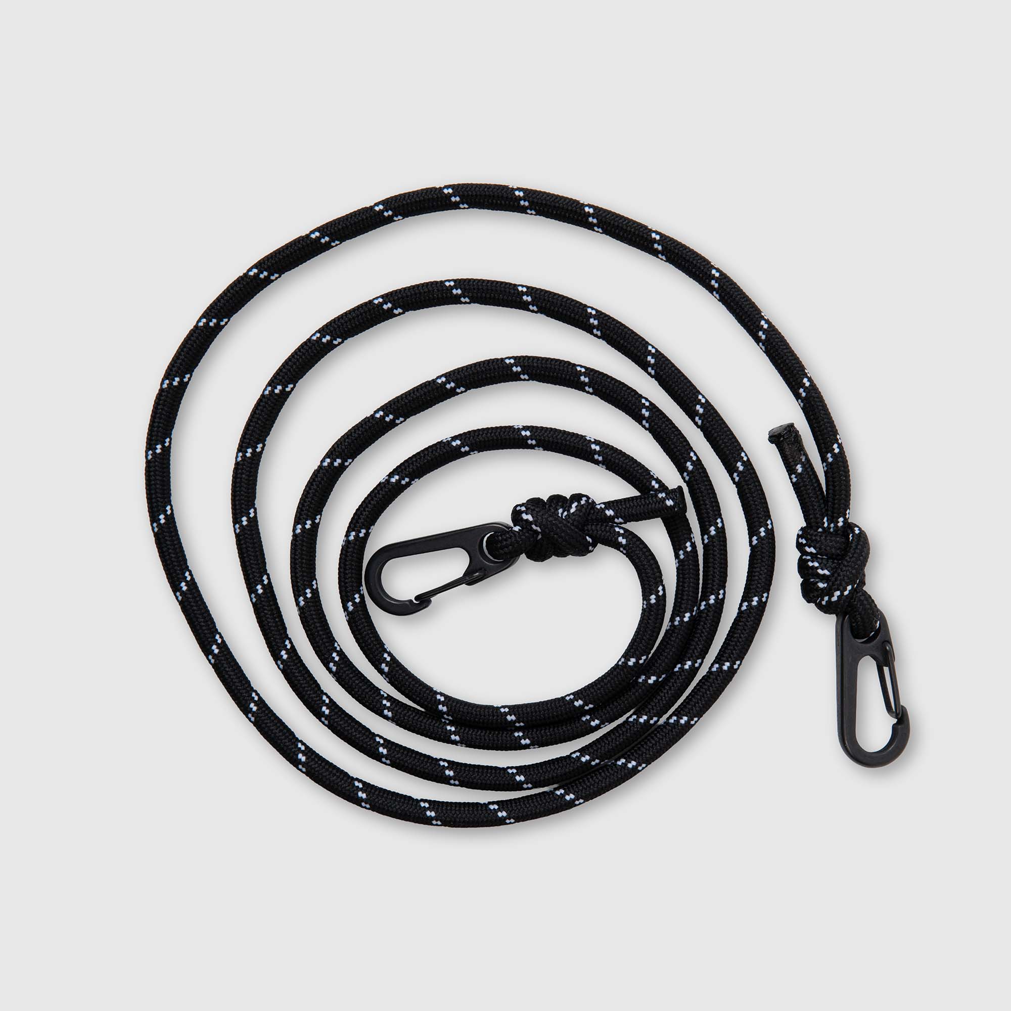 Auf einem schlichten hellgrauen Hintergrund ist ein gewendeltes schwarzes Seil mit weißen Akzenten und Metallklammern an beiden Enden abgebildet. Der „Delfonics Shoulder Strap Cord for Inner Carrying“ von Delfonics ist ein vielseitiger, verstellbarer Nylon-Trageriemen – perfekt, um Ihre Delfonics-Inner-Carrying-Tasche oder anderes Zubehör individuell anzupassen.