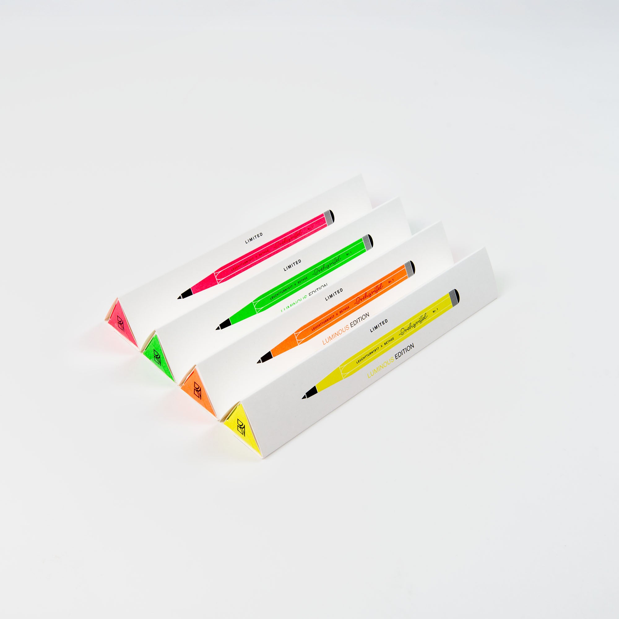 Vier Leuchtturm 1917 Drehgriffel No. 1 Luminous Edition Kugelschreiber in Pink, Grün, Orange und Gelb werden in passenden dreieckigen weißen Halterungen in einer Reihe auf weißem Hintergrund präsentiert.