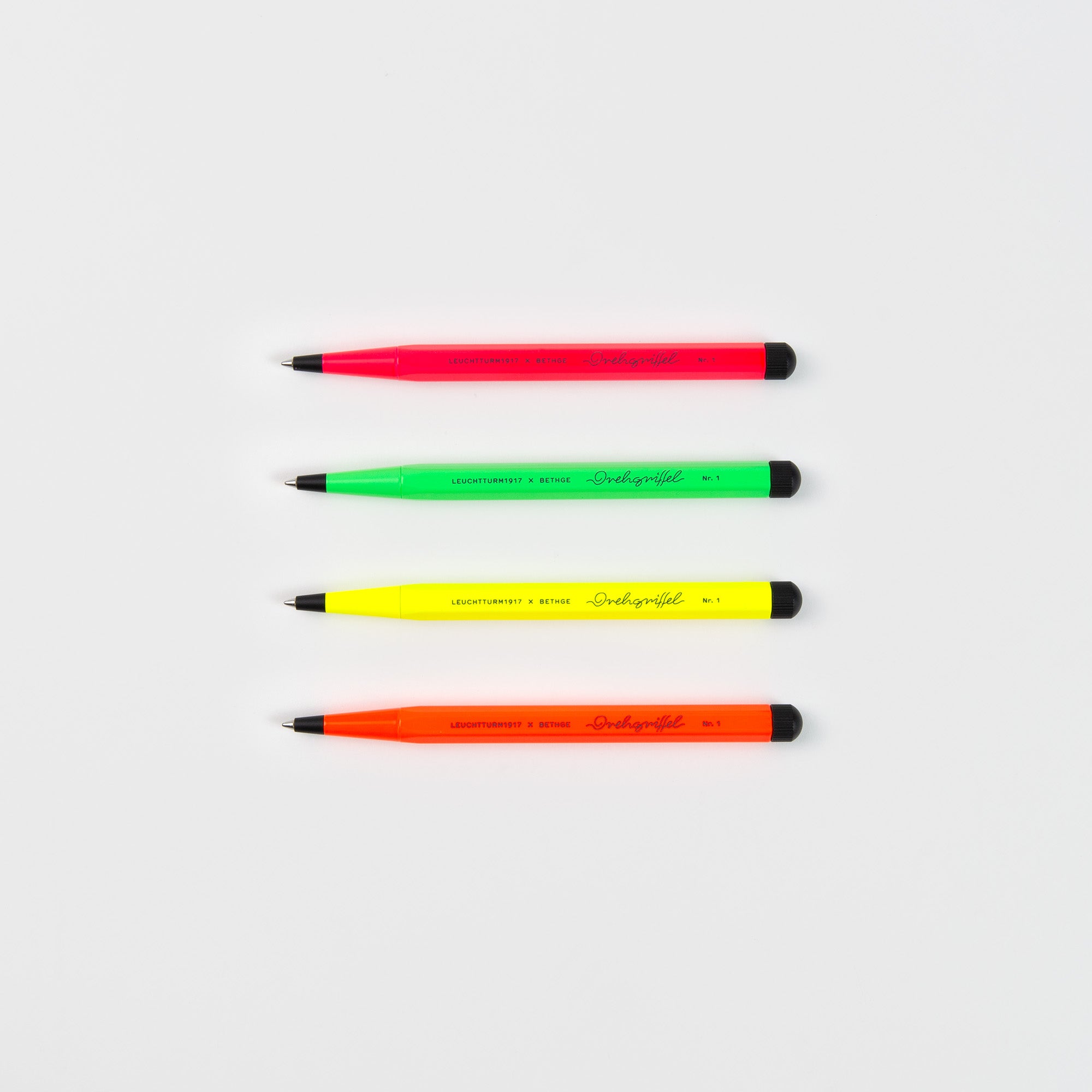 Vier Leuchtturm1917 Drehgriffel No. 1 Luminous Edition Kugelschreiber in Pink, Grün, Gelb und Orange sind horizontal auf weißem Grund angeordnet und jeweils mit schwarzen Spitzen, Clips und Klickern ausgestattet.