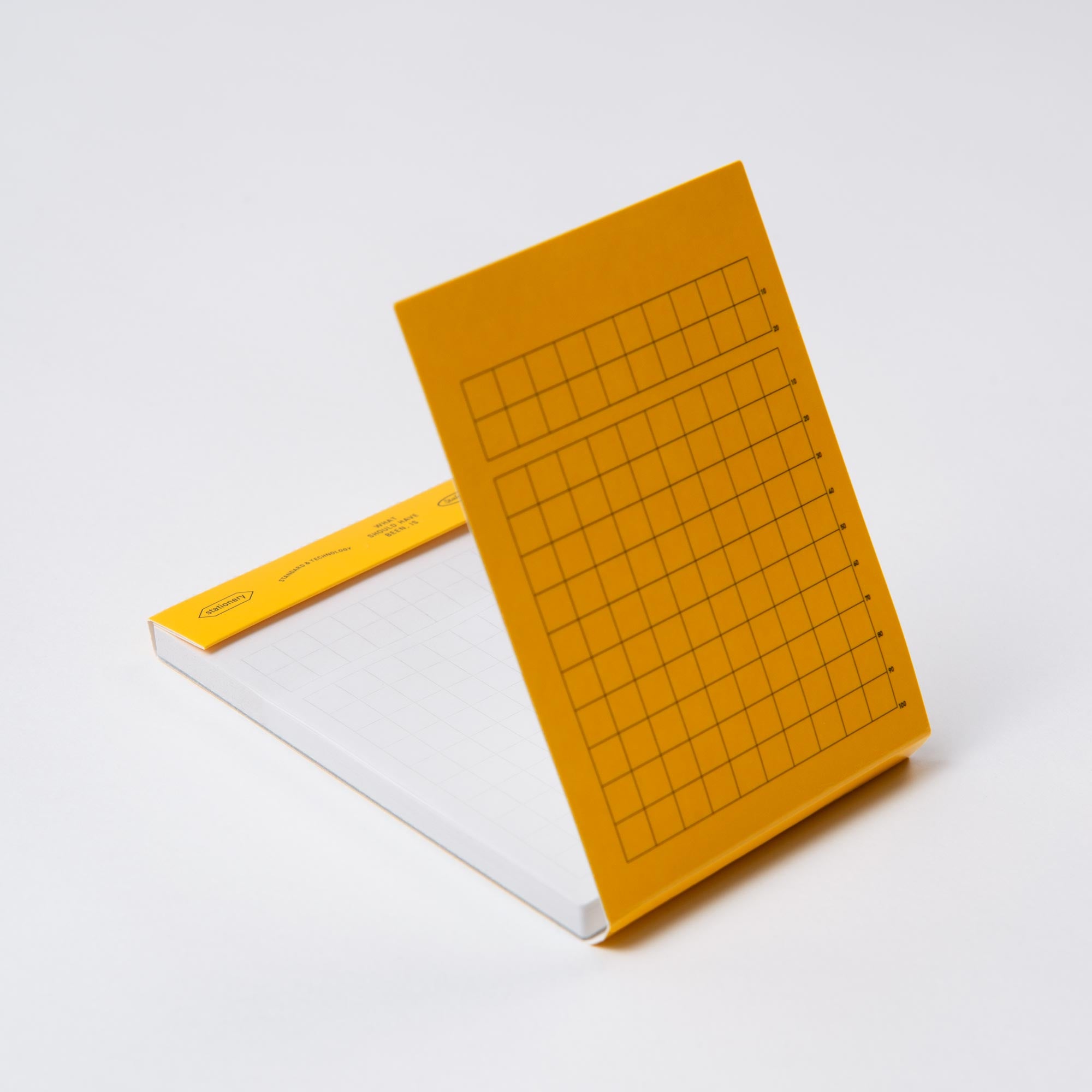 Das Stalogy Editors Memo Pad hat einen gelben Einband mit einem Gittermuster auf den Seiten, ähnlich der Editors Series. Dieser kleine Notizblock ist teilweise geöffnet und zeigt aufwendig gestaltete Gitterblätter auf einem schlichten weißen Hintergrund.