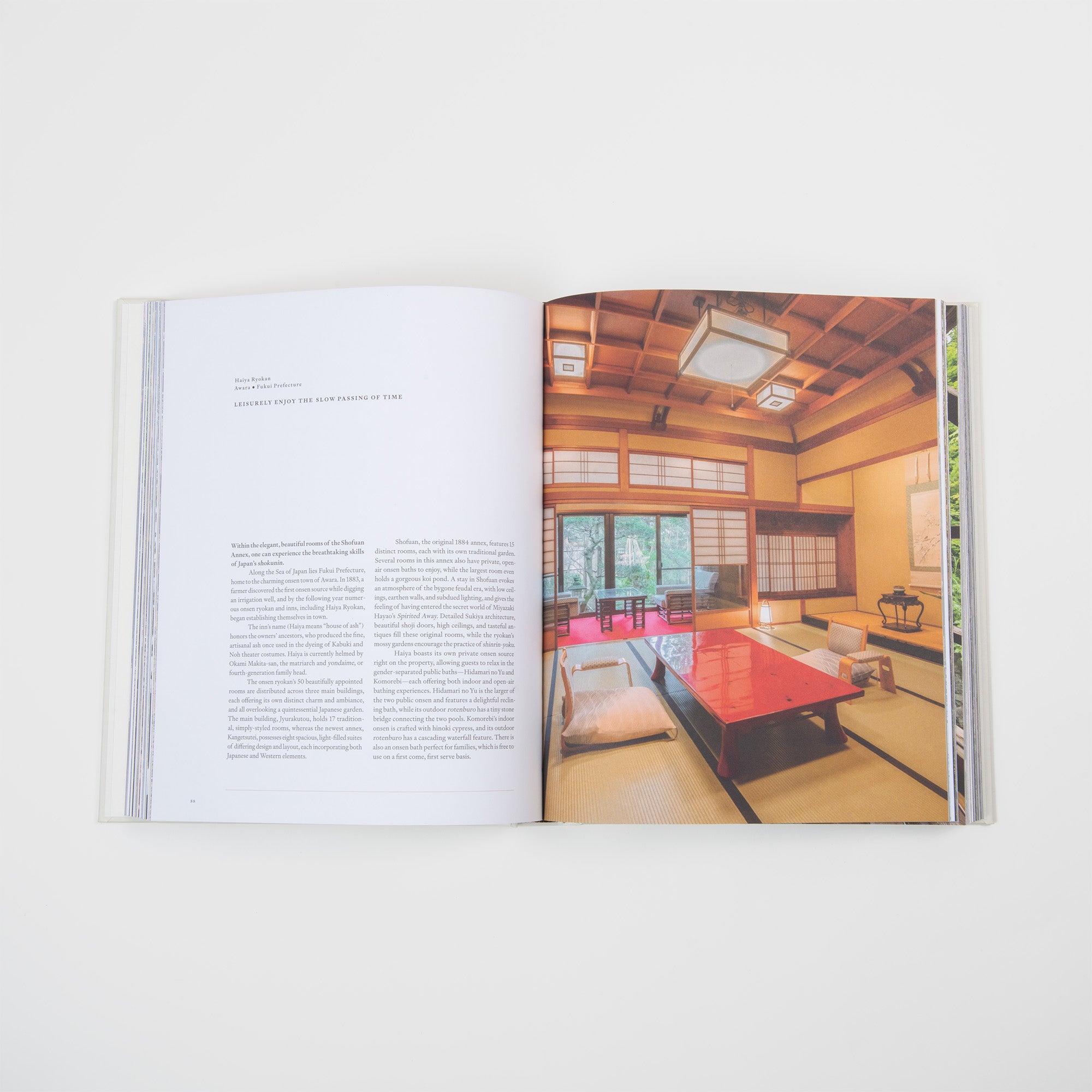 Ein aufgeschlagenes Buch aus dem Gestalten Verlag "Onsen & Ryokan of Japan - Ein Blick in Japans stille Welten" zeigt eine Textseite und ein Foto, das einen traditionellen Tatami-Raum mit niedrigen Tischen, Kissen, Papierschiebetüren und japanischer Gastfreundschaft zeigt.