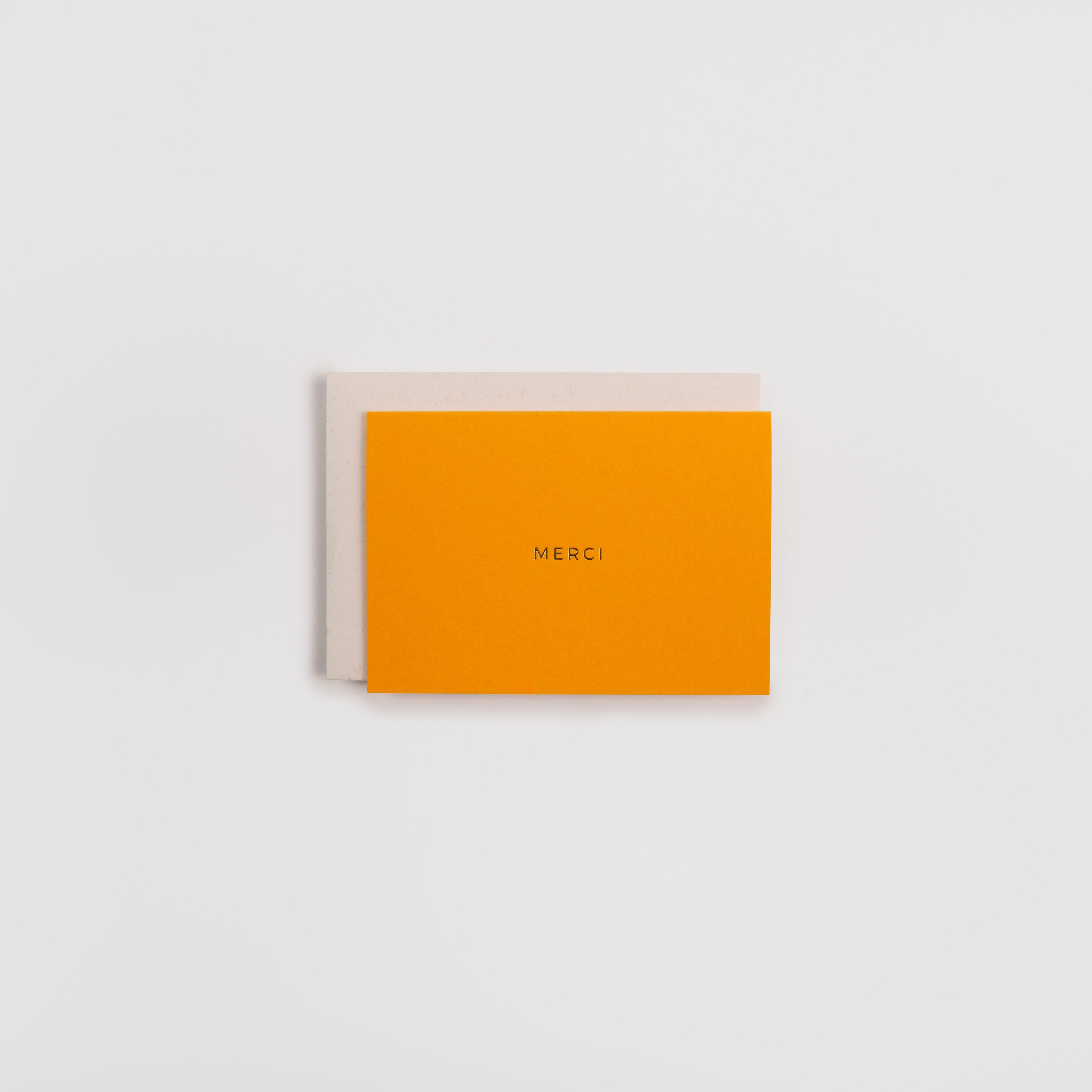 Die Karte Kärtchen MERCI von Gmund besteht aus leuchtend orangefarbenem Papier mit goldenem MERCI-Schriftzug. Sie ist auf einem schlichten hellbeigen Gmund Naturpapier-Umschlag vor einem sauberen weißen Hintergrund abgebildet.