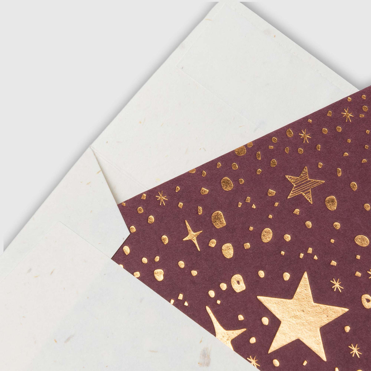Ein weißer Umschlag, der teilweise geöffnet ist und den Blick auf eine dunkelrote Gmund-Kärtchen-Karte Sternenglanz mit goldfolierten Sternen und gesprenkelten Mustern freigibt.