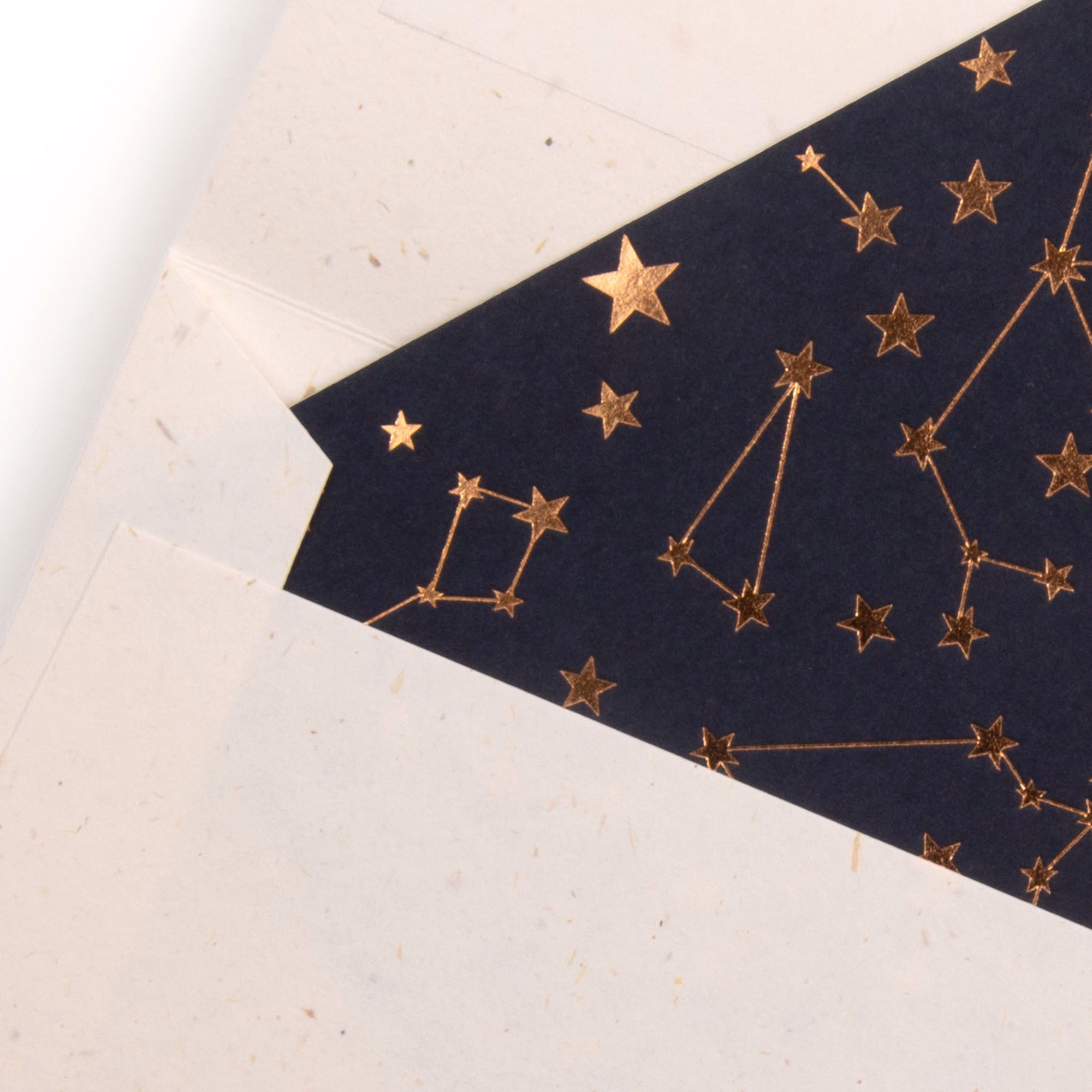 Ein teilweise geöffneter Umschlag enthüllt das Gmund Himmelskärtchen, eine dunkle, marineblaue Karte, die mit Sternbildern und Sternen aus Goldfolie verziert ist und ein himmlisches Muster zeigt.