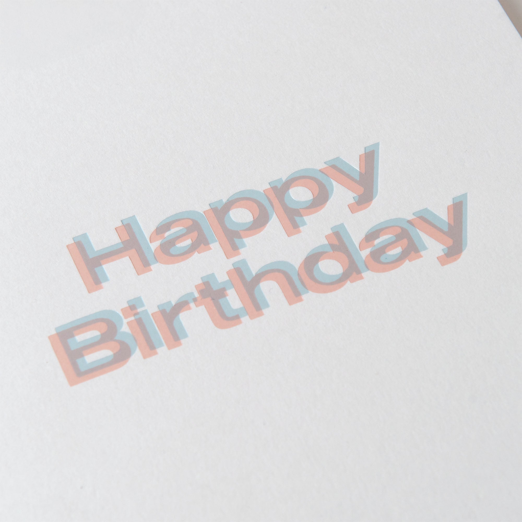 Das Bild zeigt die Happy Birthday Karte A5 von paperlux.store mit kräftigen pastellblauen und rosafarbenen, sich überlappenden Buchstaben mit Schatteneffekt - ideal für stilvolle Geburtstagskarten oder kreative Buchbindungsprojekte.
