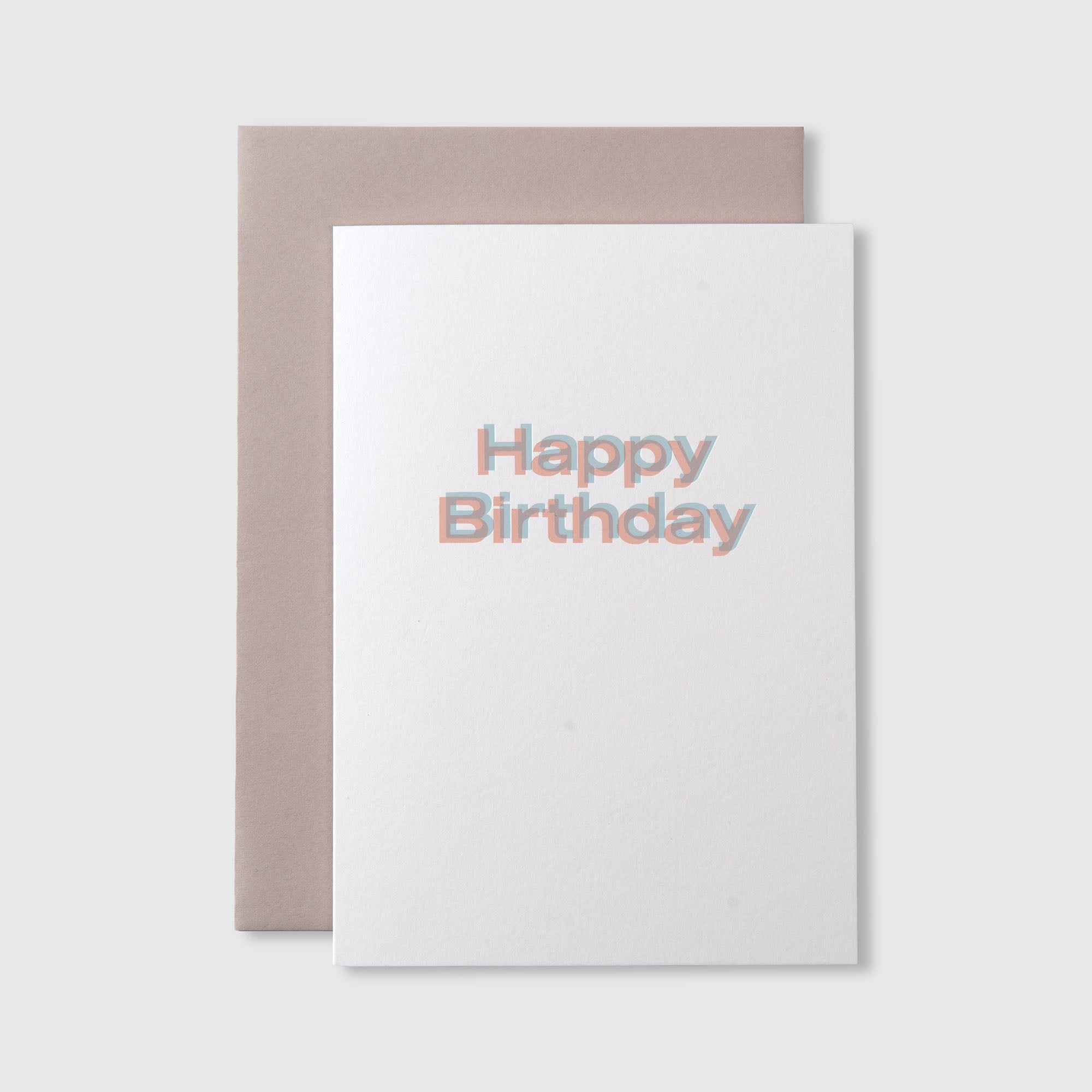 Die Happy Birthday Karte A5 von paperlux.store zeigt einen fetten, pastellfarbenen Happy Birthday Text im Buchbinderei-Stil auf einer weißen Karte, gepaart mit einem beigen Umschlag und vor einem hellgrauen Hintergrund.