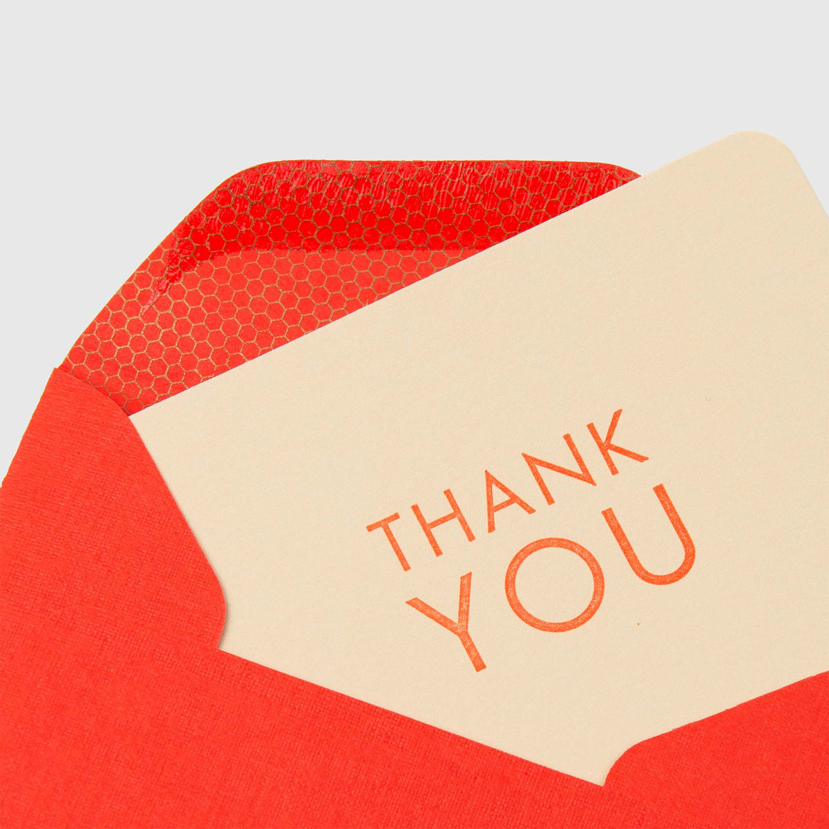 Eine wunderschön gestaltete Le Typographe Mini-Karte „Thank You“ – Cappuccino  Geranium aus cremefarbenem Karton mit orangefarbenem „THANK YOU“-Schriftzug, die teilweise in einen leuchtend roten Umschlag mit Sechseckmuster geschoben ist, der mit traditionellen Drucktechniken hergestellt wurde.