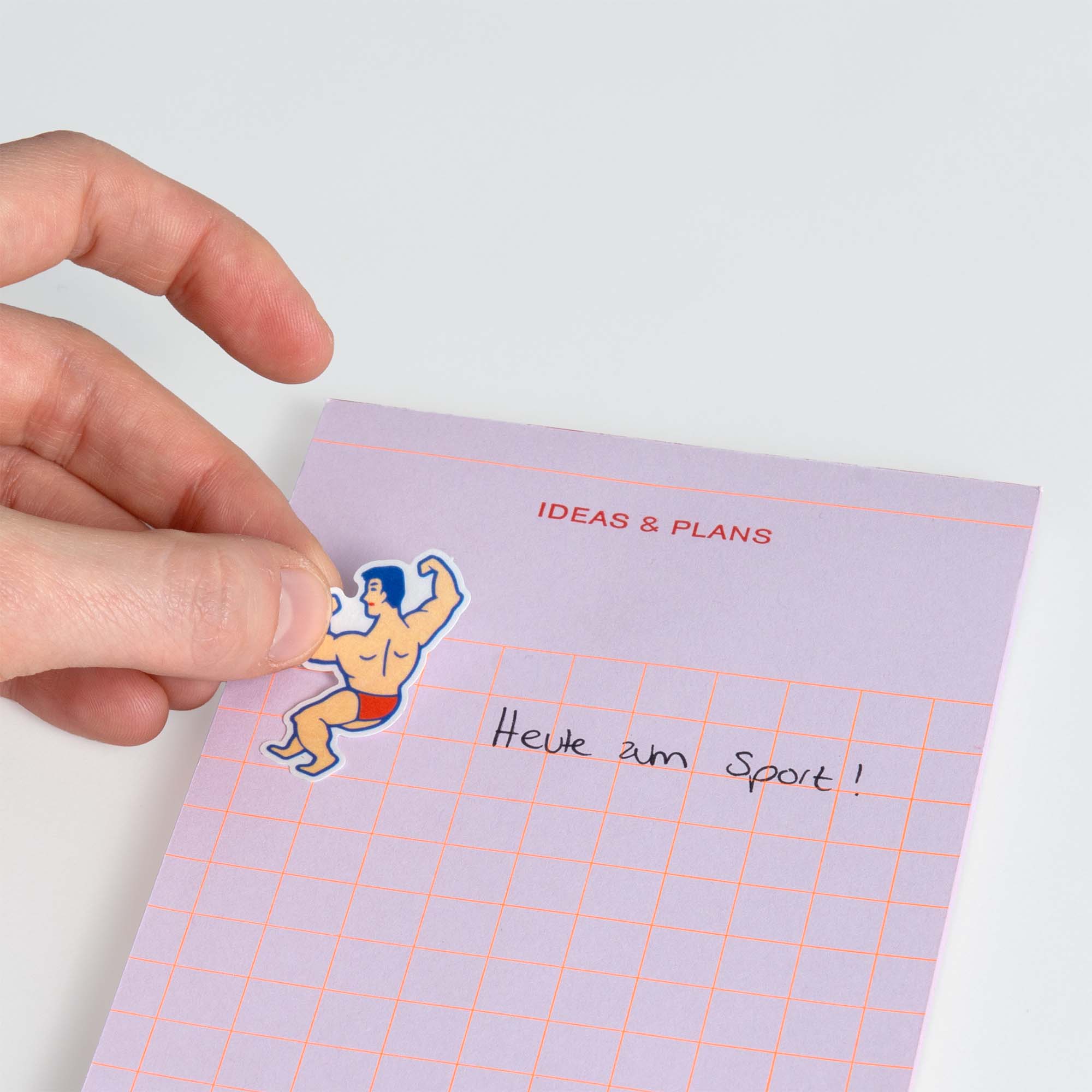 Eine Hand platziert einen Hightide Flake Sticker von Hightide, der einen sich beugenden Bodybuilder zeigt, auf einem pastellfarbenen lila Notizblock mit der Aufschrift IDEEN & PLÄNE" und der Aufschrift Heute zum Sport!" in schwarzer Tinte.