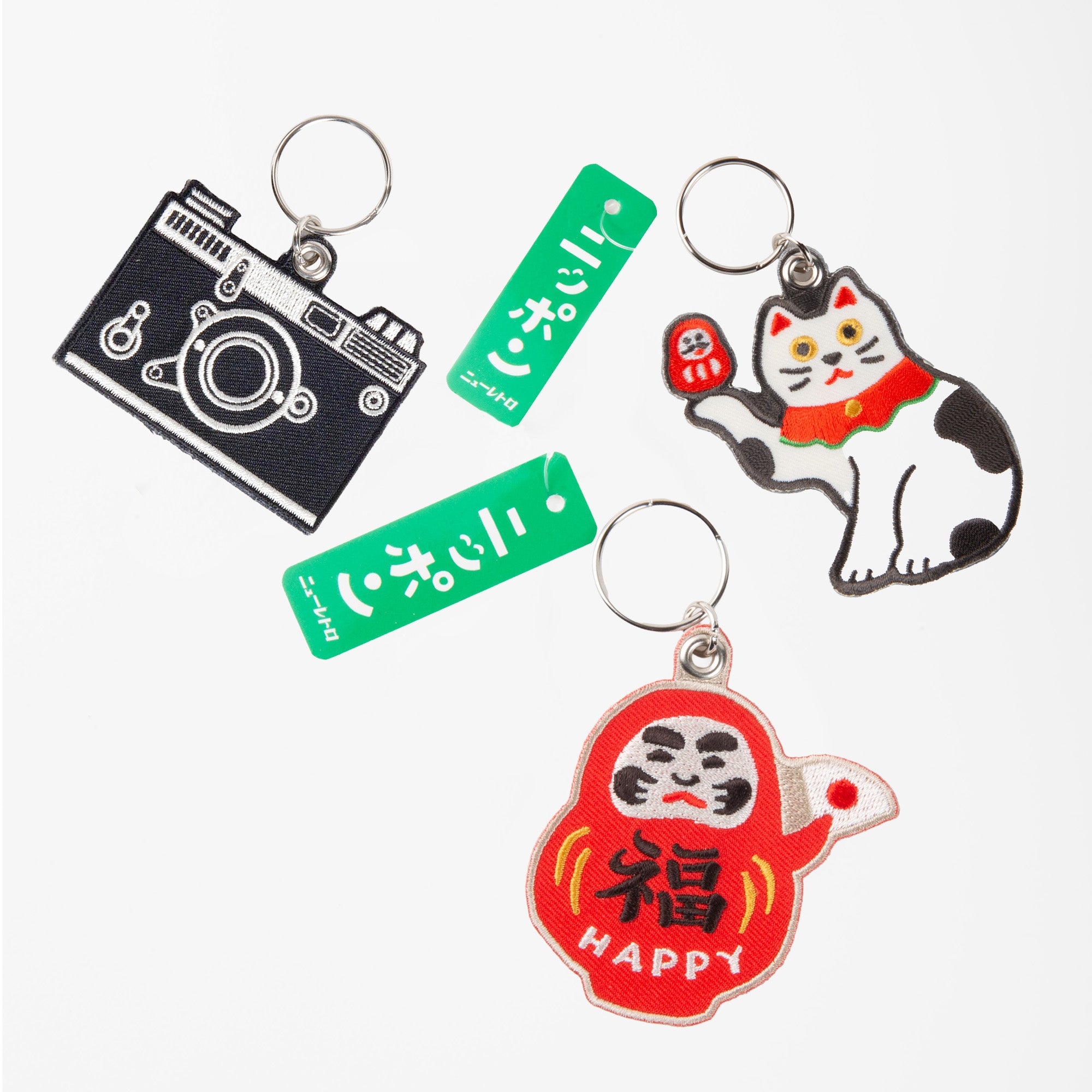 Vier Hightide Stitch Work Keychains von Hightide - Kamera, Daruma, Glückskatze und grüner Schriftzug auf weißem Hintergrund - perfekt als Geschenk oder bestickter Schlüsselanhänger im Japan-Design.