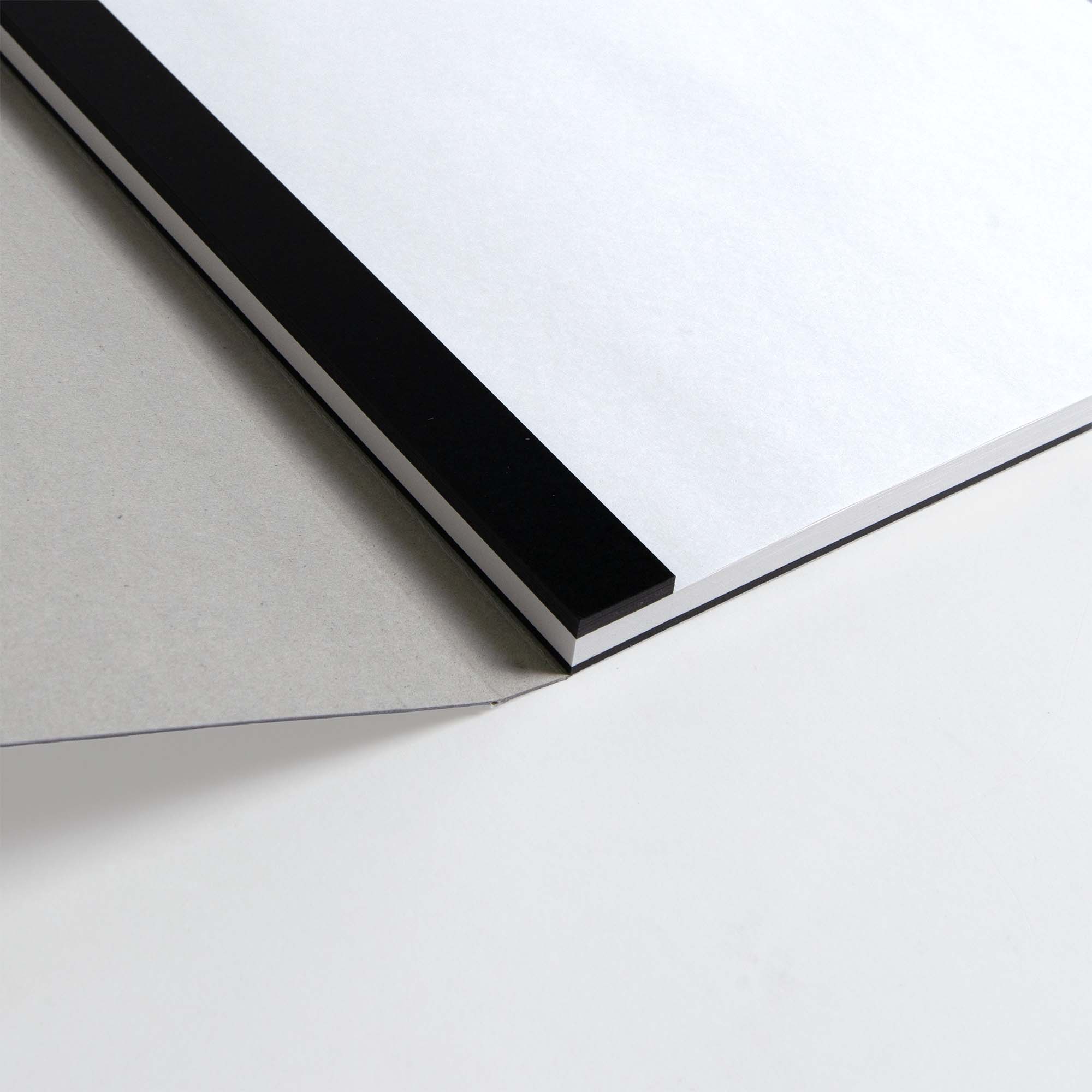 Nahaufnahme der Ecke eines ITO Bindery Drawing Pad Black Mount von ITO Bindery mit weißen Seiten und einem grauen Rückendeckel, der auf einer weißen Fläche liegt.