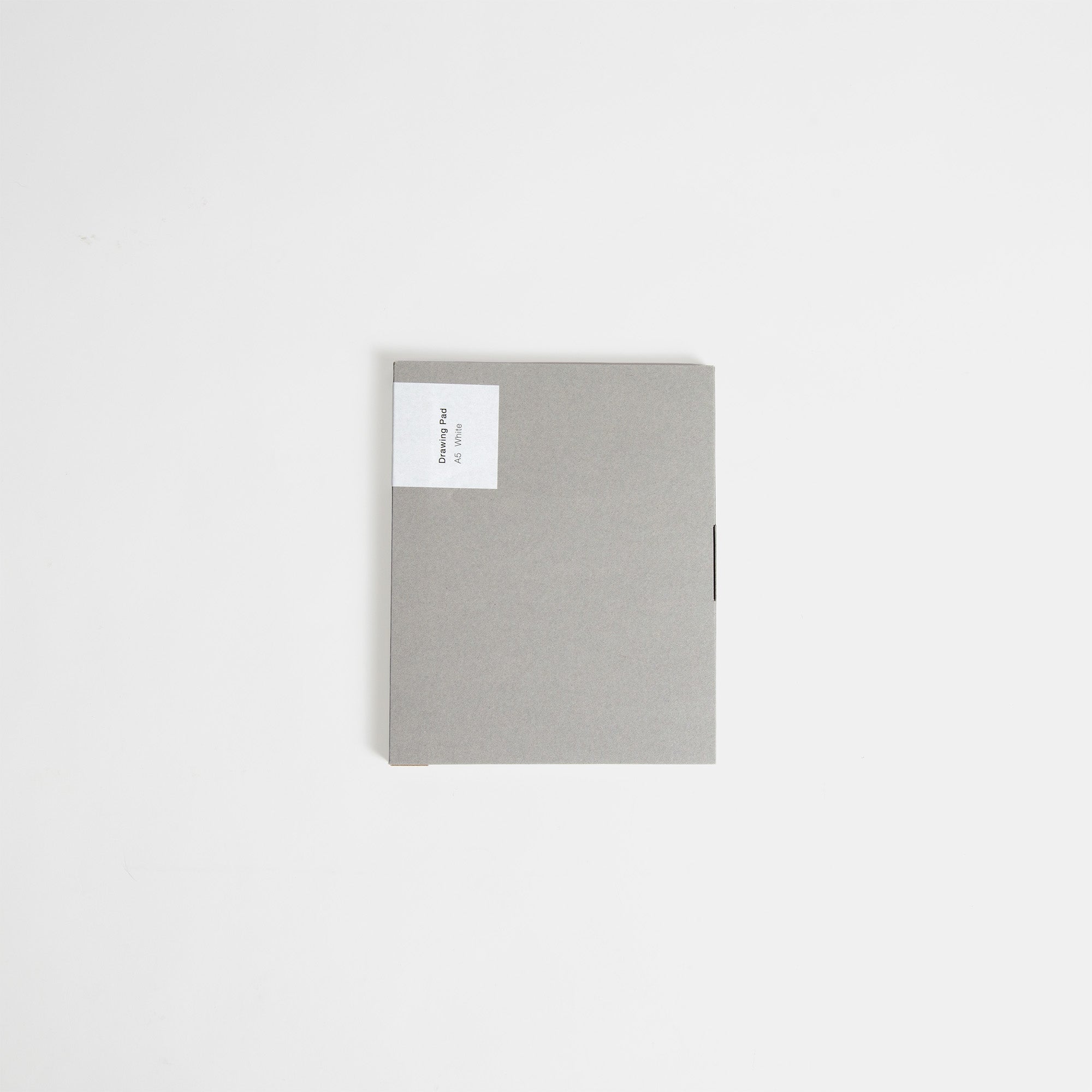 Das ITO Bindery Drawing Pad White, ein geschlossenes graues Notizbuch mit einem kleinen weißen Etikett in der linken oberen Ecke, hergestellt aus japanischem Papier von ITO Bindery, ruht auf einer schlichten weißen Oberfläche.