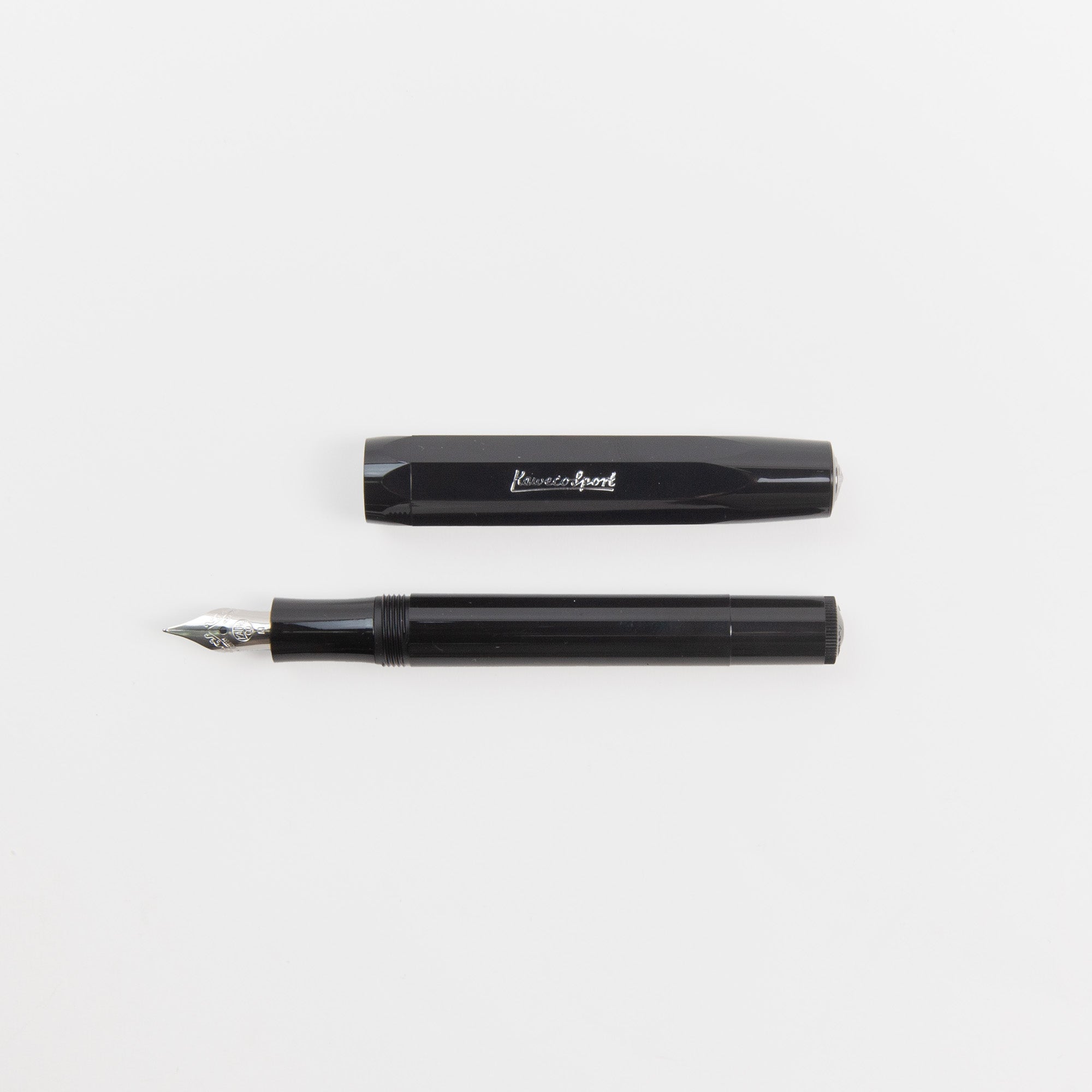 Ein schwarzer Kaweco Classic Sport - Füllhalter von Kaweco mit silberner Feder und die dazu passende Kappe sind waagerecht auf einer weißen Fläche platziert.