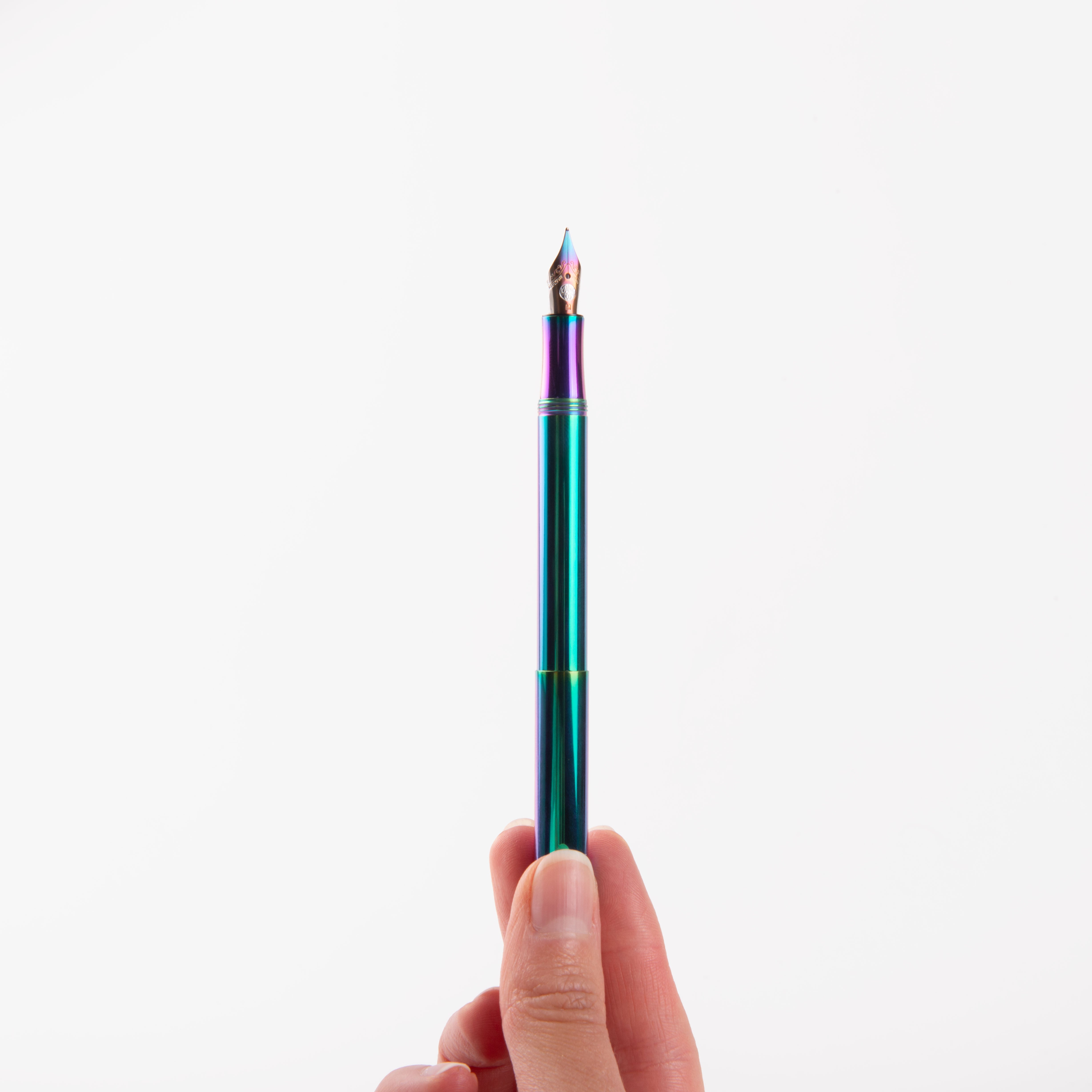Eine Hand hält den metallischen regenbogenfarbenen Kaweco Liliput Füllhalter - Kolibri Edition von Kaweco aufrecht vor einem schlichten weißen Hintergrund.
