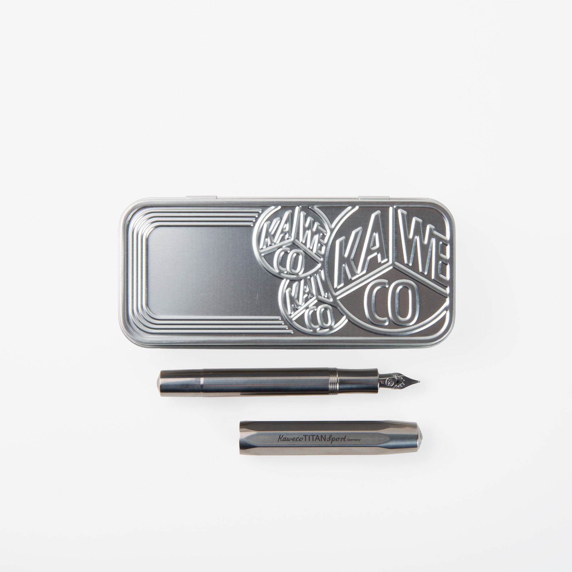 Eine metallische Blechdose mit geprägtem Kaweco-Logo liegt über einem schwarzen Kaweco Sport Füllhalter - Titan Edition, dessen Kappe abgenommen und daneben auf weißem Hintergrund platziert ist.