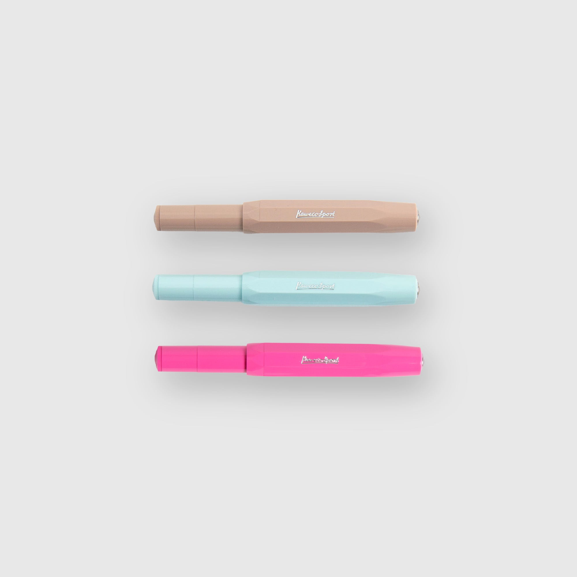 Drei Kaweco Skyline Sport - Füllhalter in braun, hellblau und rosa liegen nebeneinander auf einem hellgrauen Hintergrund. Jeder Füllhalter hat eine passende Kappe, silberne Feder, und das weiße Kaweco Logo aufgedruckt.