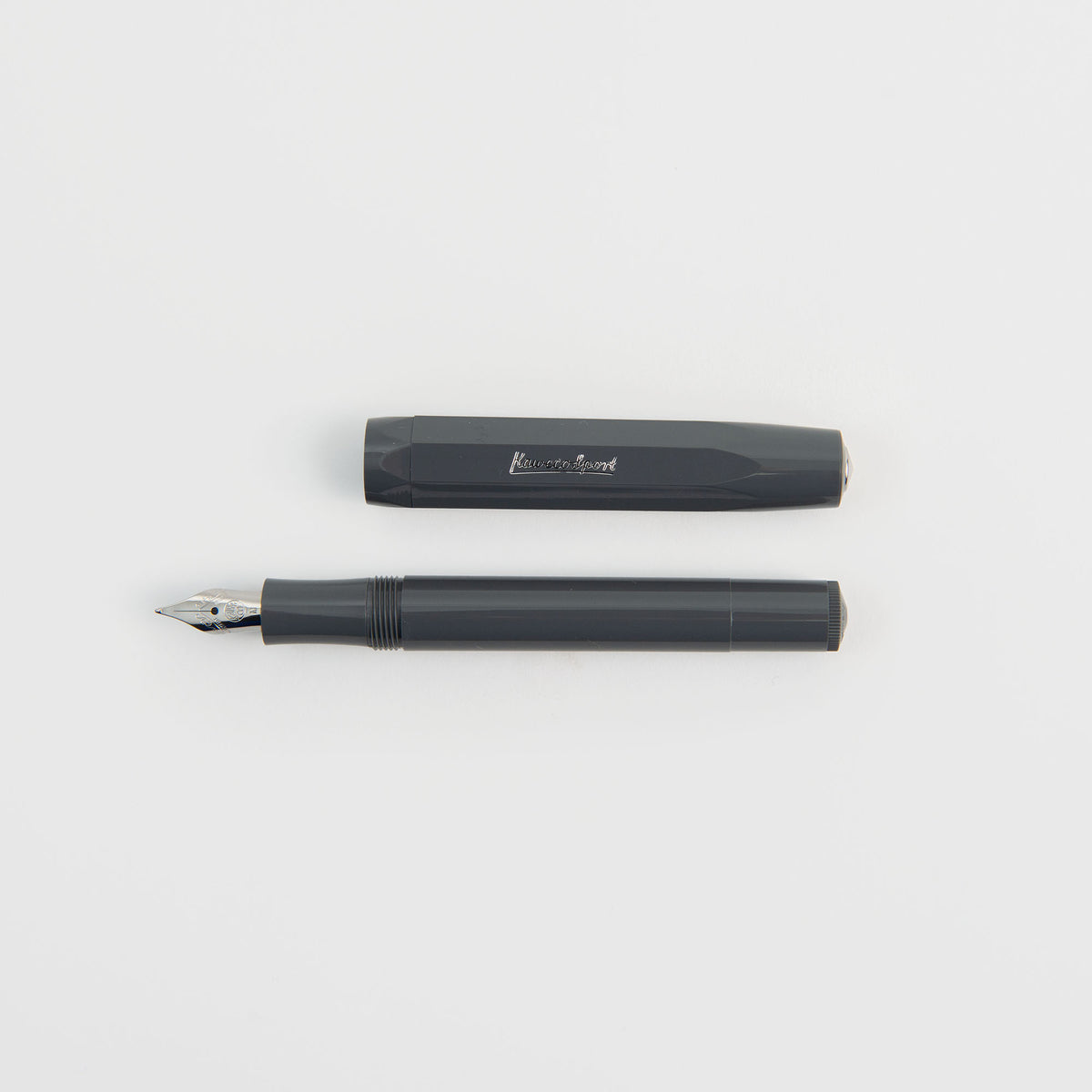 Ein grauer Kaweco Skyline Sport – Füllhalter von Kaweco, abgebildet mit abgenommener Kappe, wobei beide Teile parallel auf einer weißen Unterlage liegen. Der Füllhalter verfügt über eine silberne Feder, und die Kappe ist mit einem kleinen Metallclip versehen.