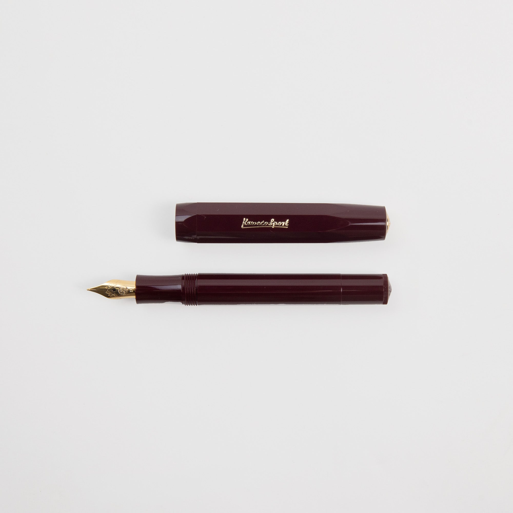 Ein weinroter Kaweco Classic Sport - Füllhalter von Kaweco mit Goldfeder liegt getrennt von seiner Kappe, beide horizontal auf einem schlichten weißen Hintergrund.