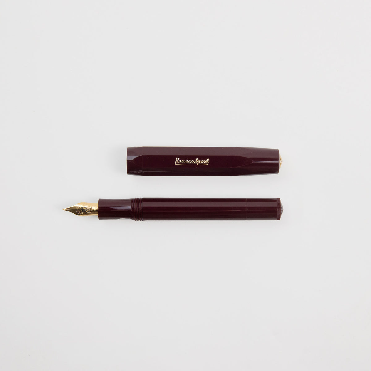 Ein burgunderroter Kaweco Classic Sport – Füllhalter von Kaweco mit einer goldenen Feder und einer passenden Kappe, beide horizontal auf weißem Hintergrund angeordnet. Die Kappe dieses Füllhalters ist mit einer goldenen Gravur versehen.