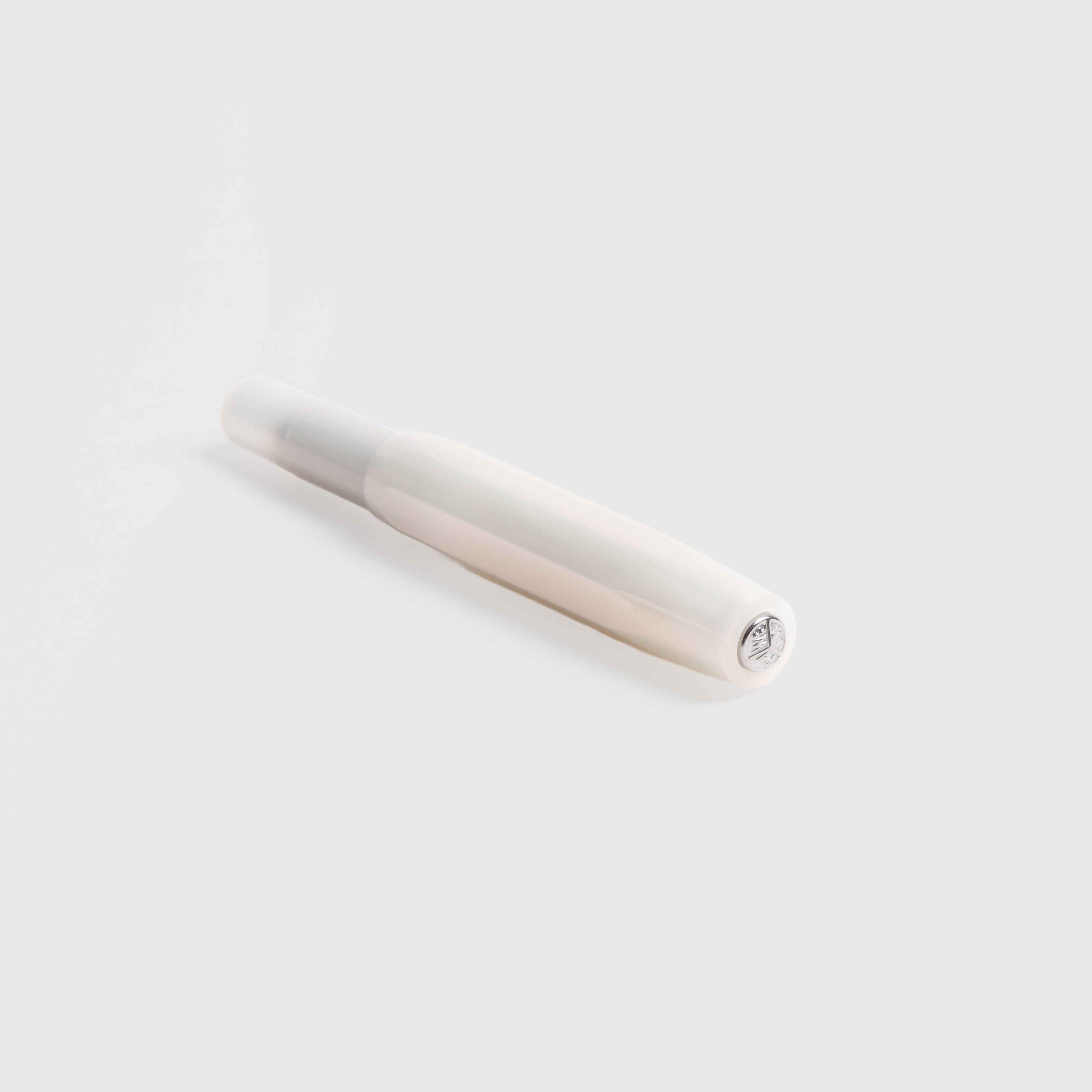Ein weißer Kaweco Lunar Sport - Kugelschreiber mit abgerundeter Kappe ruht auf einer hellgrauen Oberfläche. Sein minimalistisches Design zeichnet sich durch ein silbernes Detail am Kappenende und einen dezenten Perlglanz-Effekt aus.