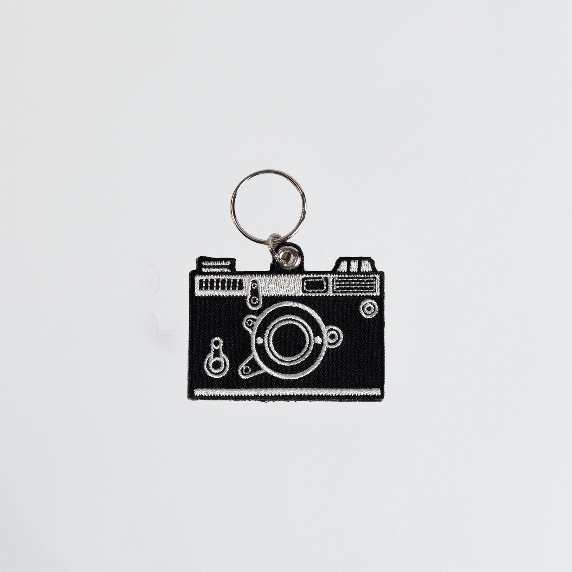 Ein Hightide Stitch Work Keychain - Kamera von Hightide zeigt eine schwarze Vintage-Kamera mit weißen Umrissen, zentriert auf einem schlichten weißen Hintergrund - ein idealer bestickter Schlüsselanhänger und Geschenk für Japan.