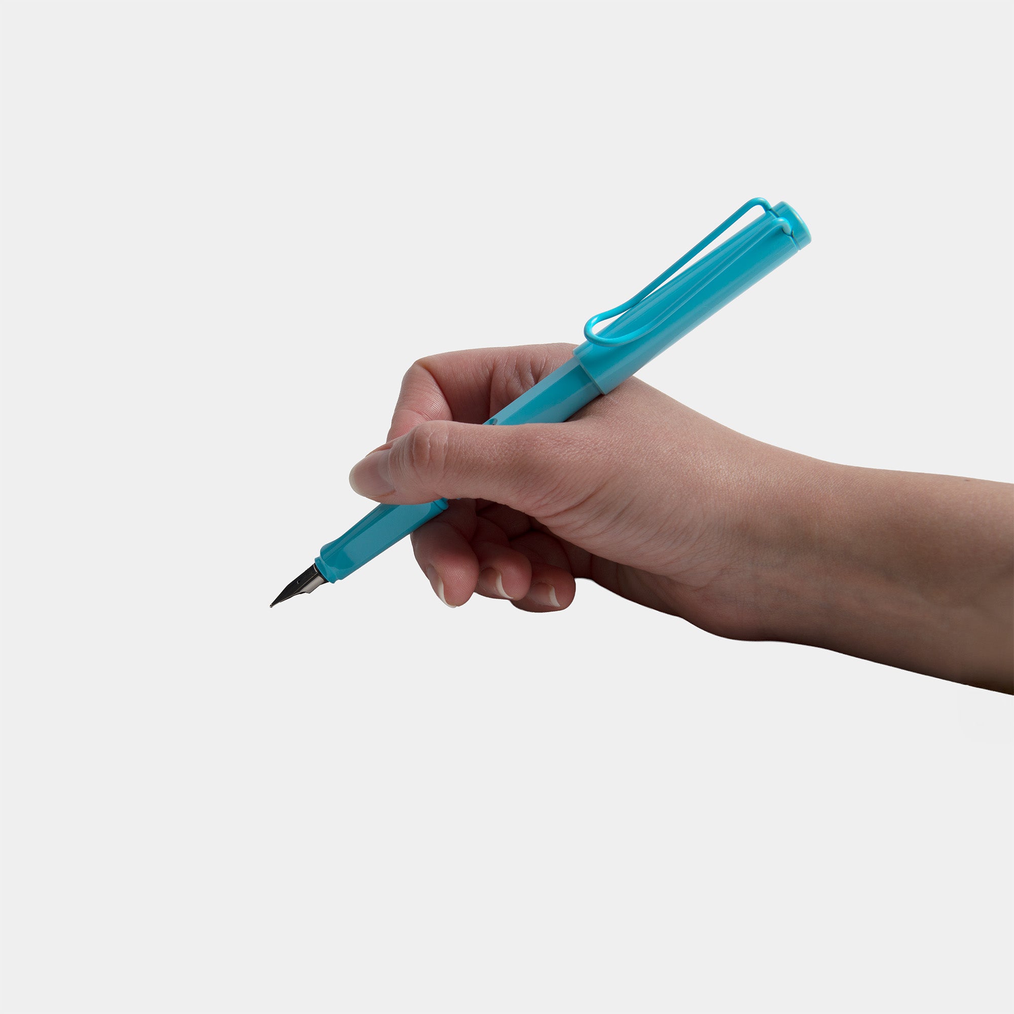 Eine Hand, die einen türkisfarbenen LAMY safari Füllhalter von Lamy, hergestellt aus ASA-Kunststoff, hält, ist bereit, vor einem schlichten hellgrauen Hintergrund zu schreiben.