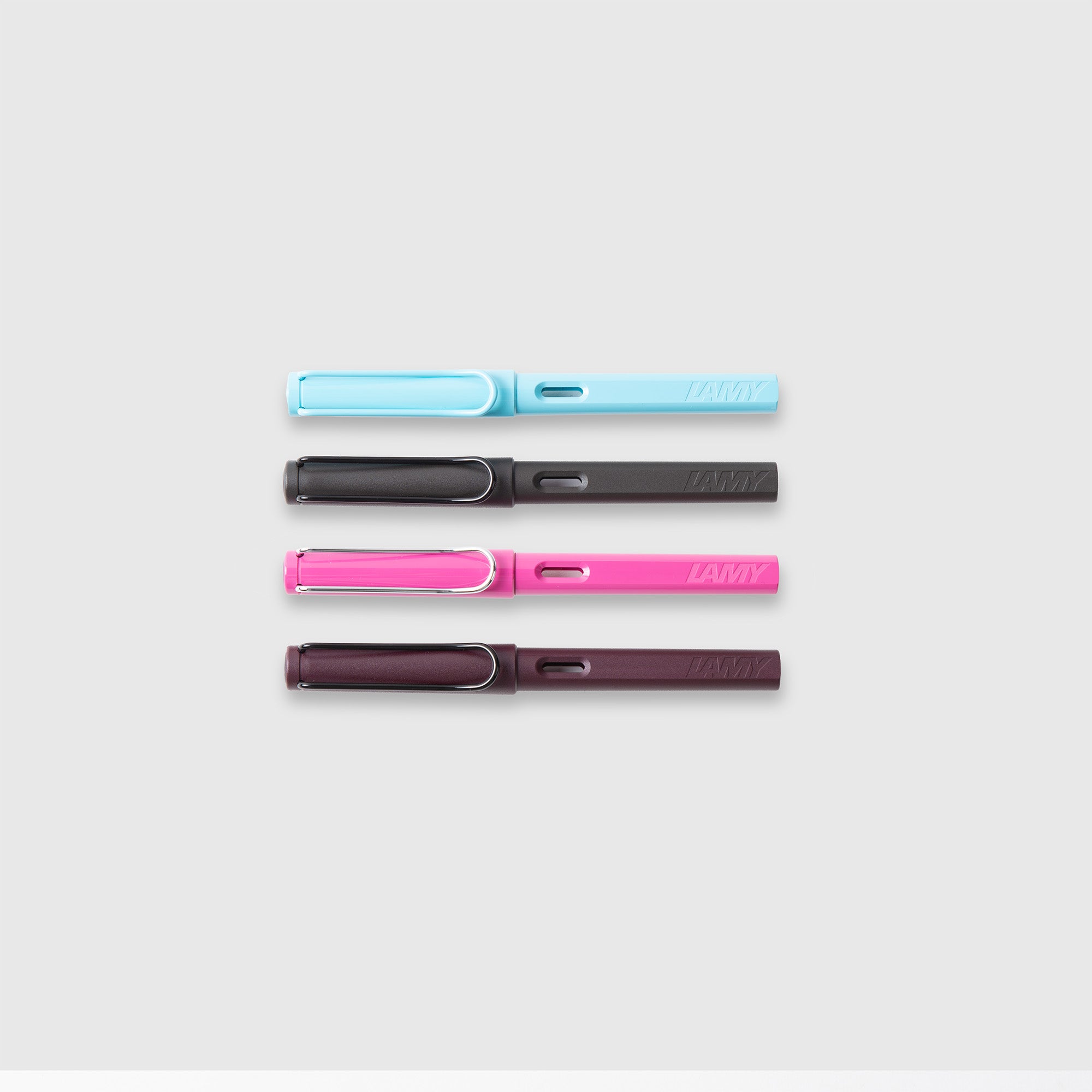 Vier LAMY safari Füllhalter von Lamy in pastellblau, dunkelgrau, hellrosa und dunkelviolett ASA-Kunststoff sind waagerecht auf einem hellgrauen Hintergrund angeordnet.