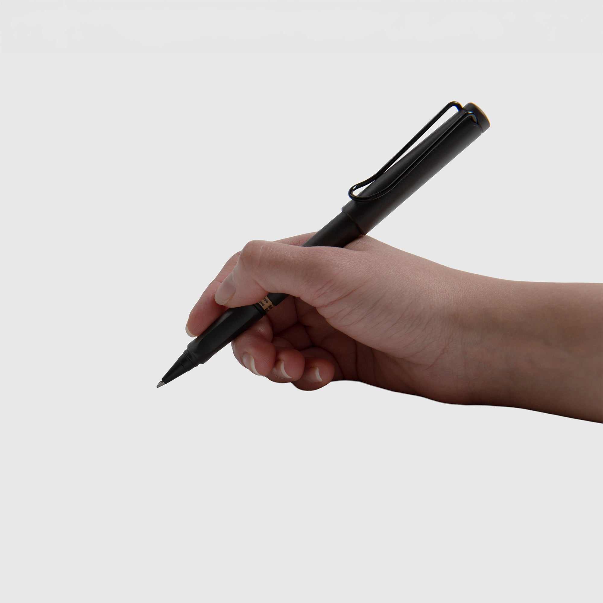 Eine Hand hält einen schwarzen LAMY safari Tintenpatronenroller - Tintenroller von Lamy mit ergonomischem Griffstück, bereit zum Schreiben, vor einem schlichten weißen Hintergrund.