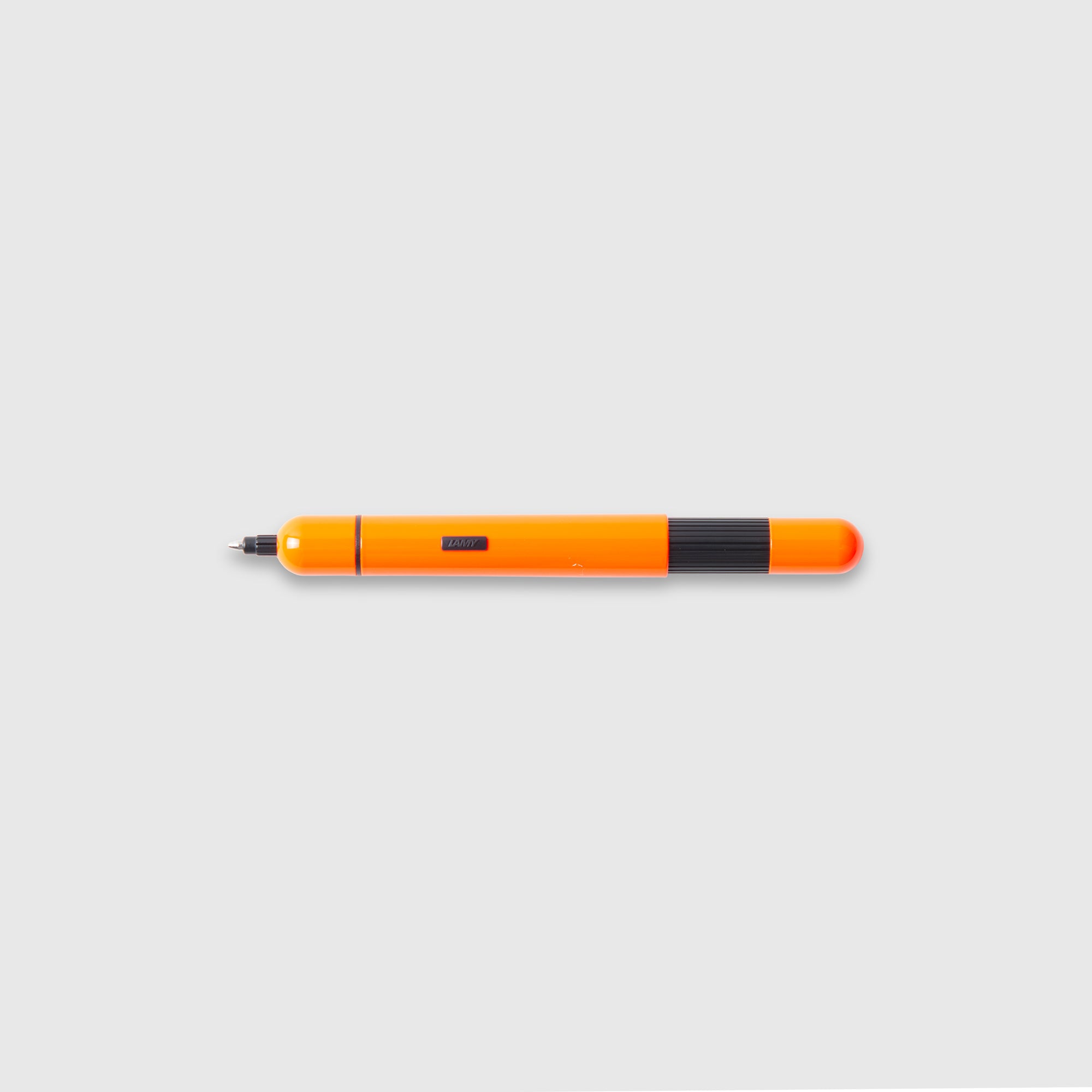 Abgebildet ist ein Lamy LAMY pico Kugelschreiber in Orange und Schwarz mit abgerundeter Kappe, der waagerecht auf einem hellgrauen Hintergrund liegt.