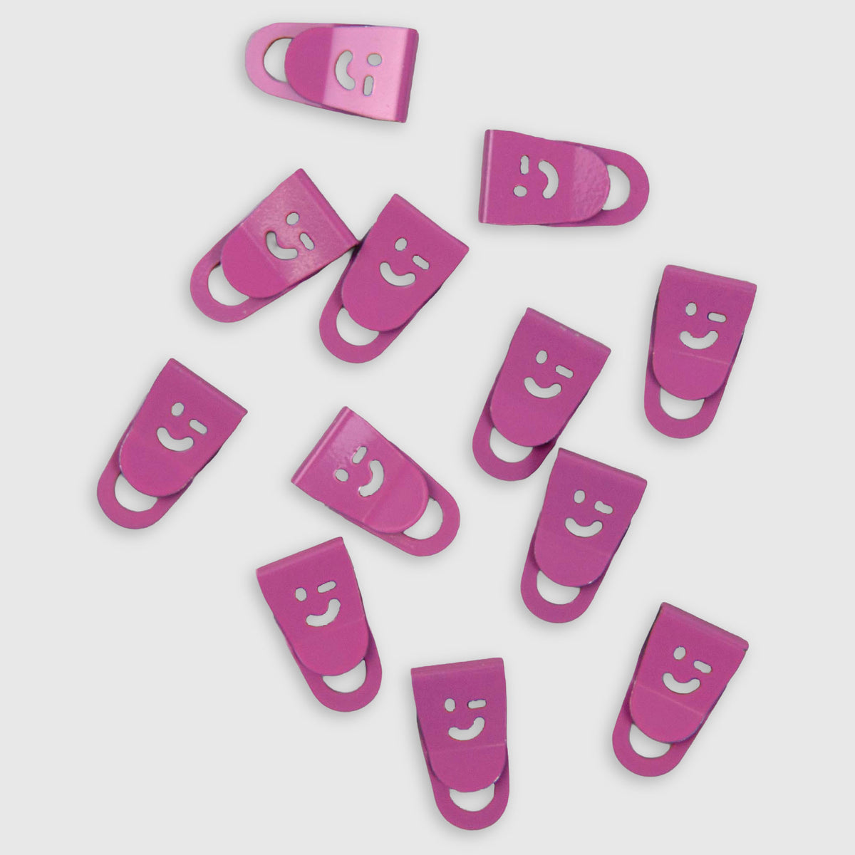 Zwölf magentafarbene Mini-Clips Smiley mit jeweils einem ausgestanzten Smiley-Motiv zur Organisation auf dem Schreibtisch.