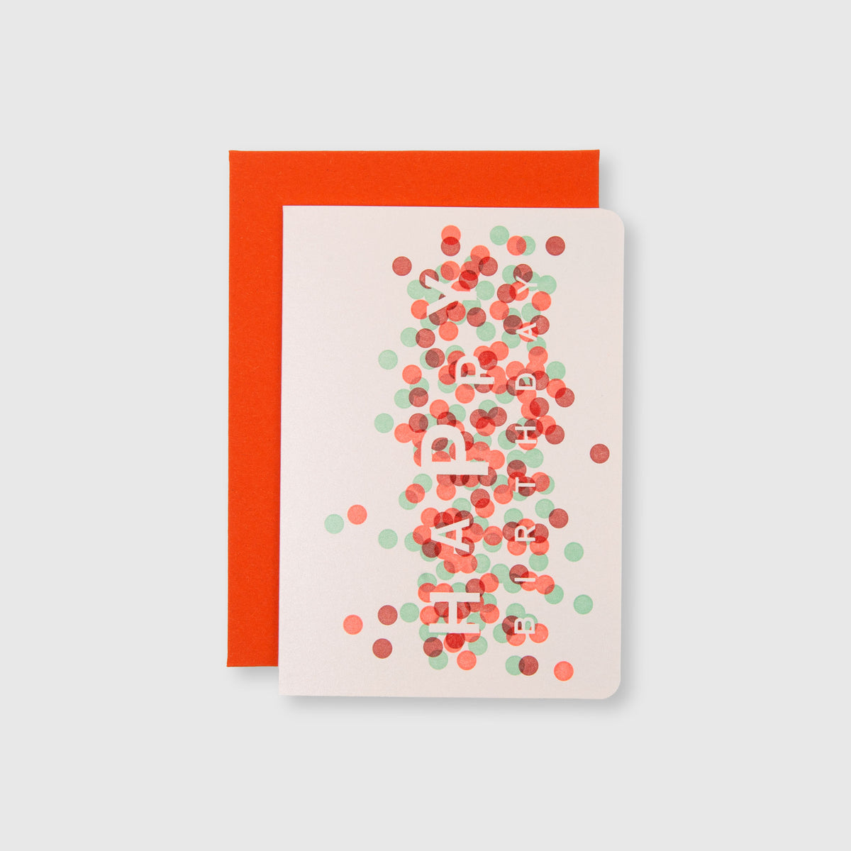 Eine weiße „HAPPY BIRTHDAY“-Konfetti-Karte und ein Umschlag von Le Typographe, auf deren Vorderseite „HAPPY BIRTHDAY“ zu lesen ist und die mit roten, grünen und rosa Konfetti-Punkten in wunderschöner Handarbeit verziert ist, liegen auf einem leuchtend orangefarbenen Umschlag.