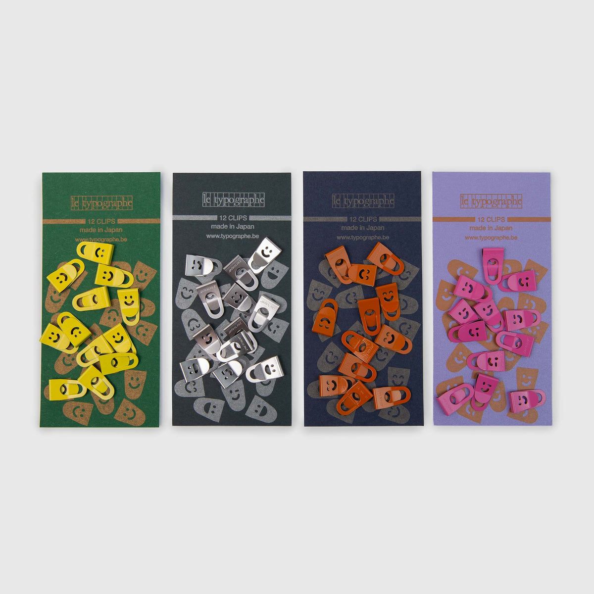 Vier Packungen Le Typographe Mini Clips Smiley, die jeweils zwölf rechteckige Metall-Heftklammern mit gelben, silbernen, orangefarbenen und rosa Smiley-Motiven enthalten.