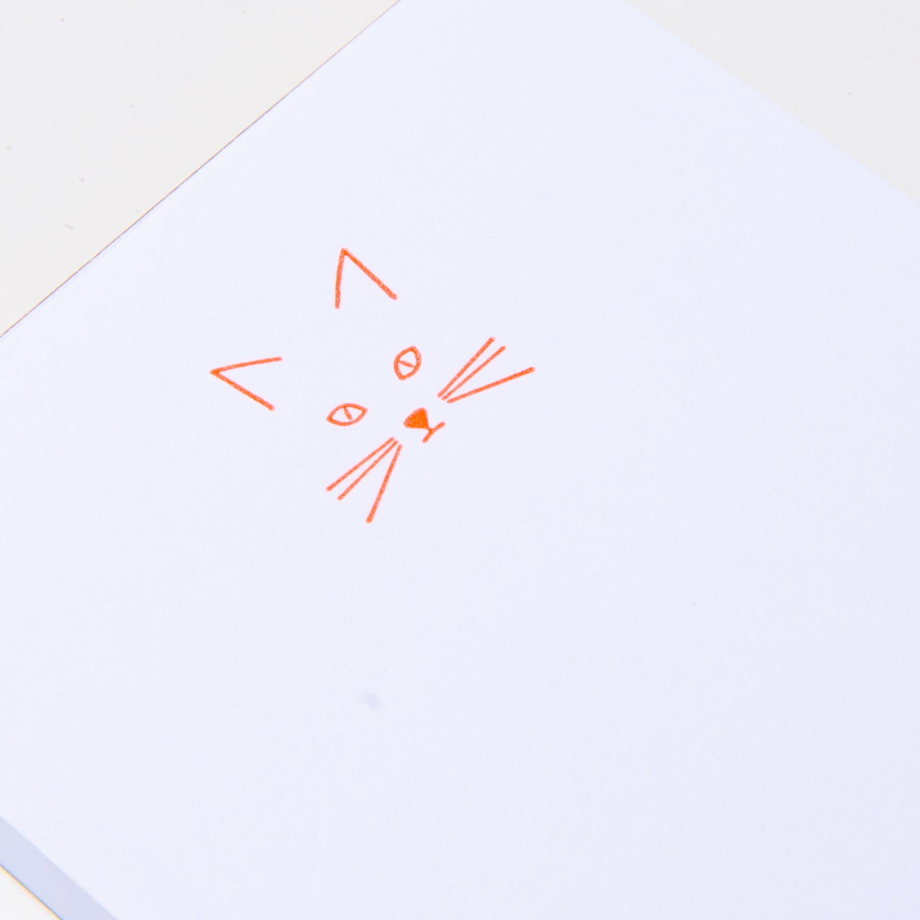 Eine schlichte orangefarbene Strichzeichnung eines Katzengesichts steht mittig auf den weißen Mini-Notizblöcken - Kiss Kiss, Love Love von Le Typographe - ideal, um schnelle Notizen oder süße Erinnerungen zu notieren.