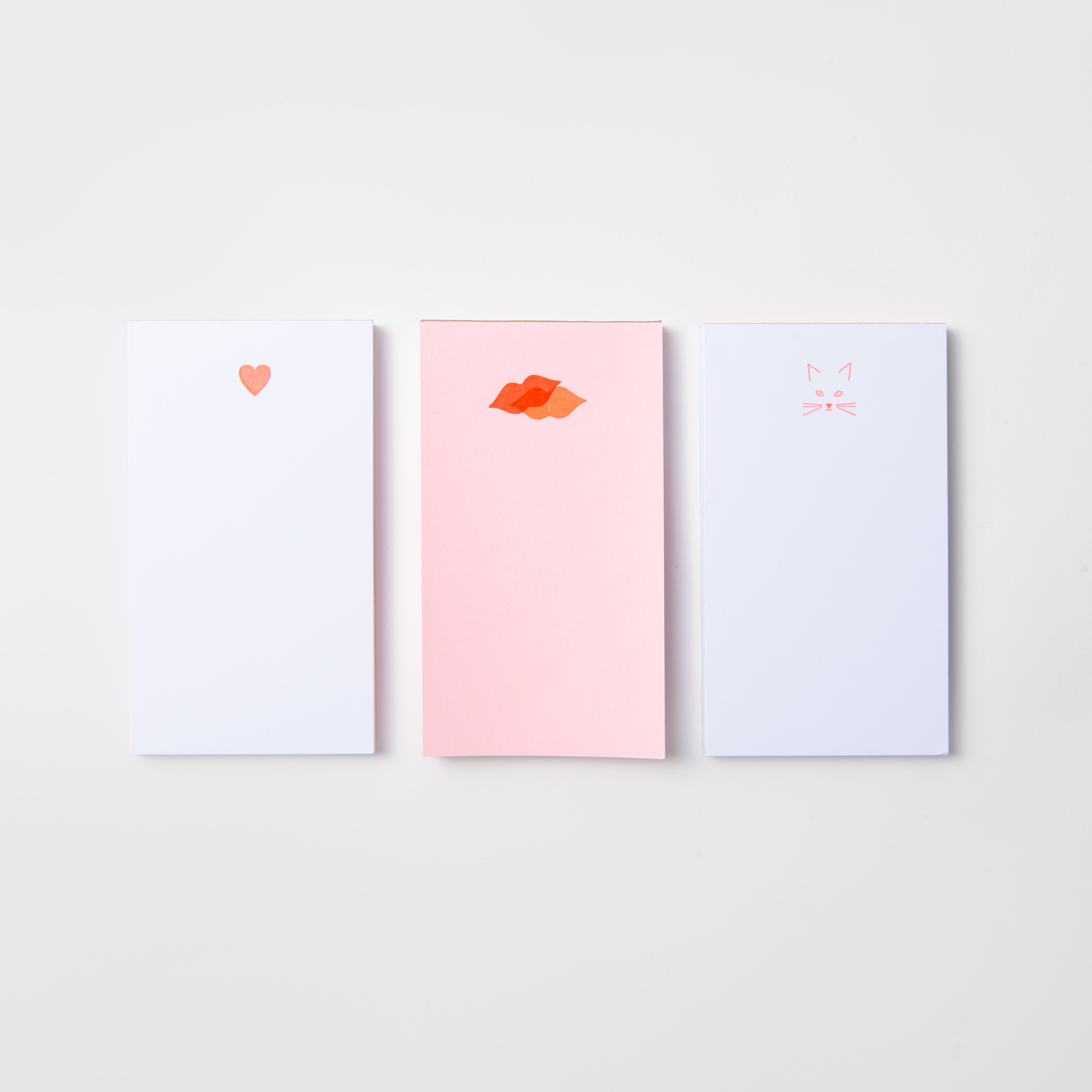 Drei minimalistische Le Typographe Mini-Notizblöcke - Kiss Kiss, Love Love sind nebeneinander abgebildet: ein rotes Herz, rote Lippen und ein rosa Katzengesicht - perfekt für kleine Liebesbekundungen.
