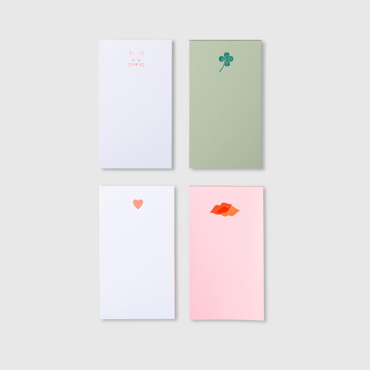 Vier Mini-Notizblöcke – Kiss Kiss, Love Love in Weiß, Hellgrün und Hellrosa, mit Illustrationen eines Katzengesichts, eines vierblättrigen Kleeblatts, eines Herzens und von Lippen.
