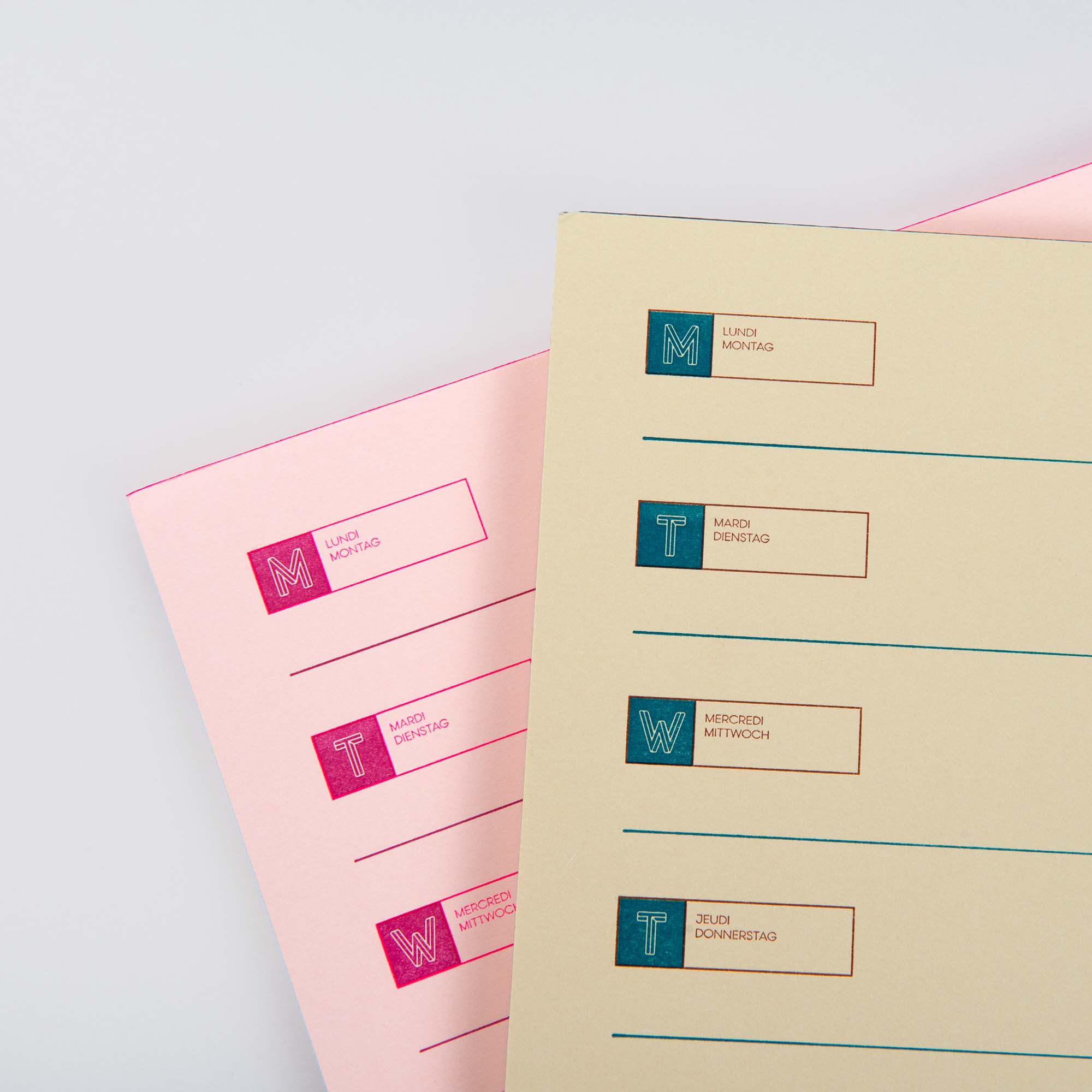 Der Le Typographe Desk Diary Horizontal verfügt über zwei horizontale A4-Wochenplanungsblätter in deutscher Sprache. Jede Zeile beginnt mit einem farbigen Anfangsbuchstaben und dem Namen des Wochentags auf rosa und cremefarbenen Seiten, die alle auf einem weißen Hintergrund stehen.