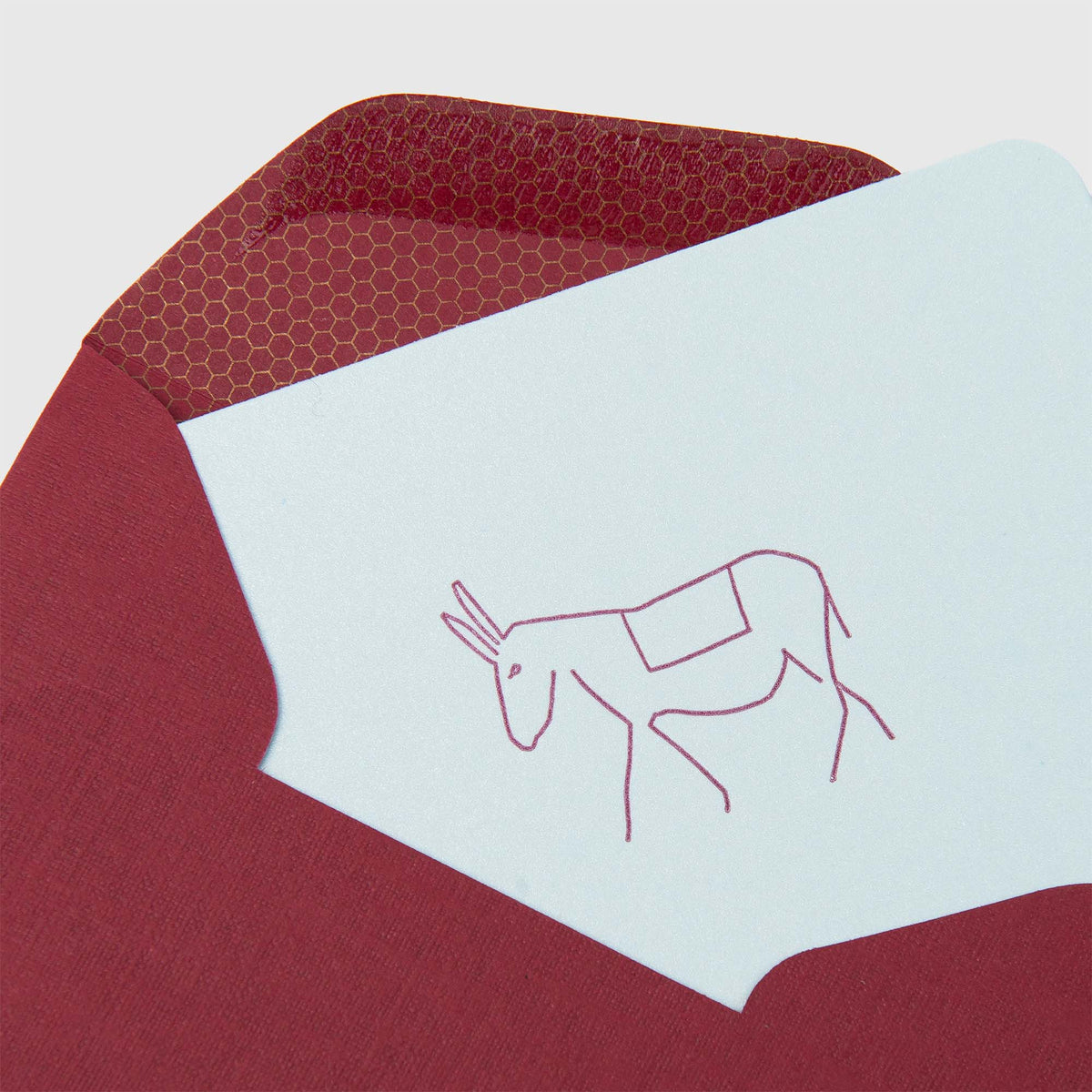 Eine weiße Mini-Karte „Esel“ von Le Typographe, verziert mit einer minimalistischen, rot umrandeten Illustration eines Esels, ist teilweise in einen roten Umschlag gesteckt, dessen Innenklappe mit einem Sechseckmuster verziert ist – ein raffiniertes Detail, das die Buchdruckkunst der Marke unterstreicht.