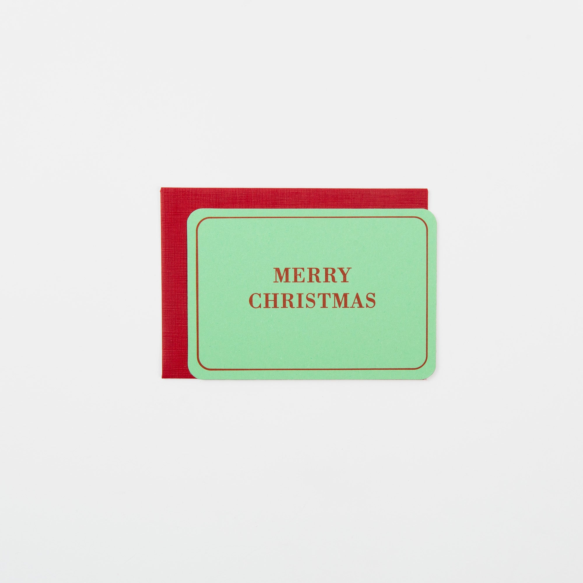 Die "Merry Christmas - Mini Karte" von Le Typographe: minimalistisch in Grün mit goldenen Rändern und edler Letterpress-Prägung, präsentiert auf rotem Umschlag vor weißem Hintergrund.