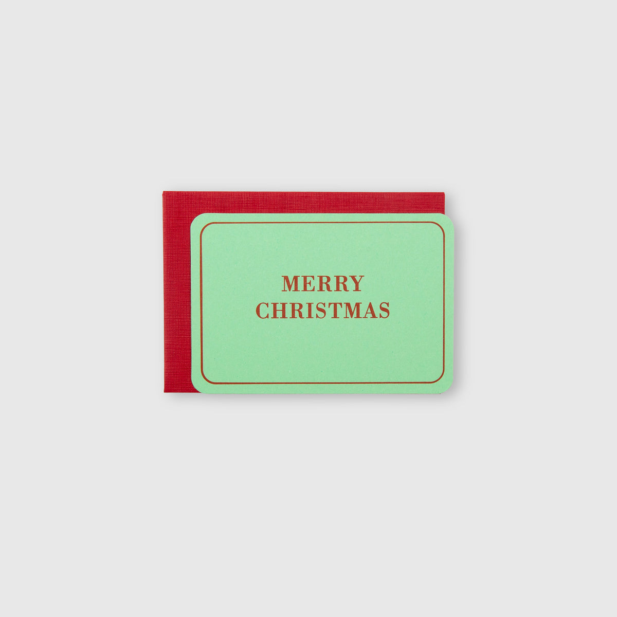 Minimalistisches Weihnachtsgruß-Set – Minikarte mit dem Schriftzug MERRY CHRISTMAS in Braun, die auf einem dunkelroten Umschlag liegt.